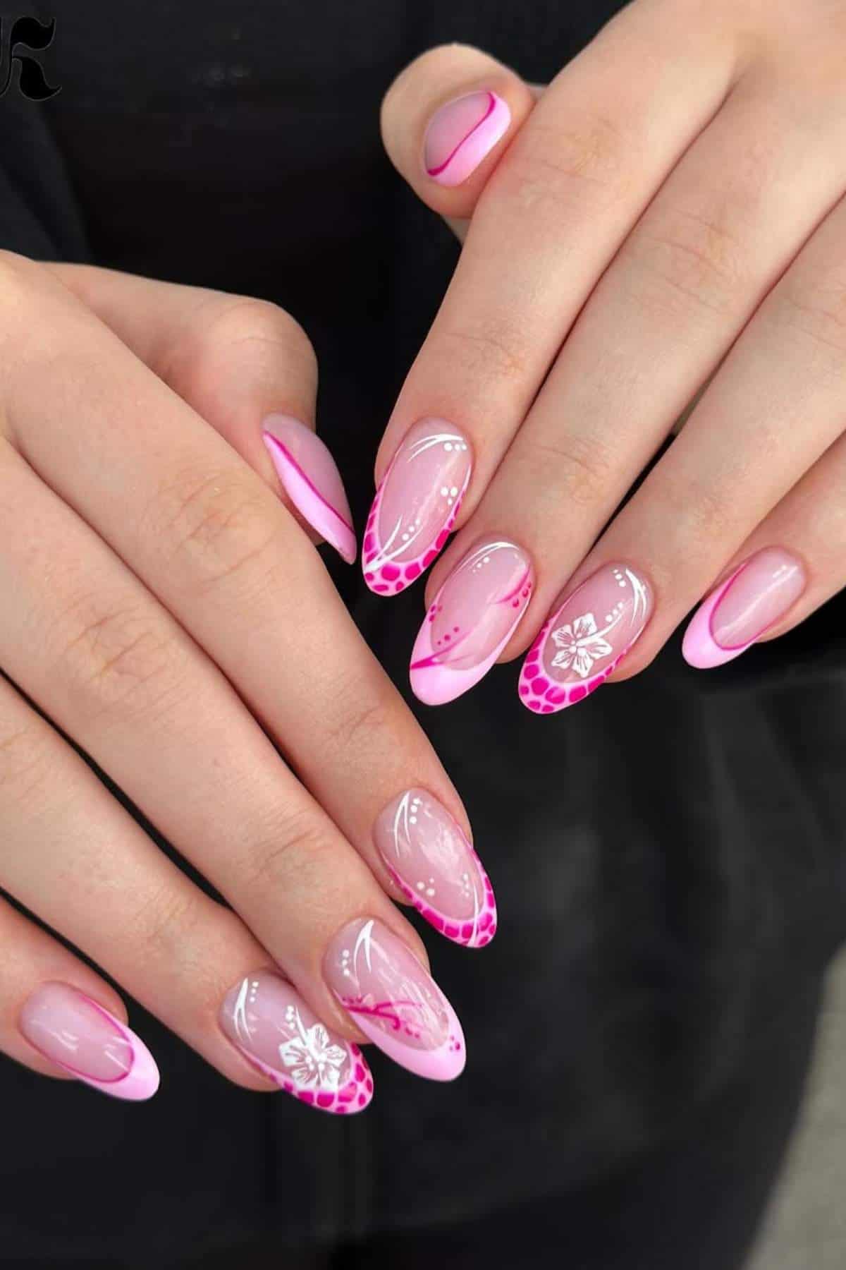 Hands with almond-shaped nails featuring pink French tips, white floral designs, and detailed pink patterns on a neutral background.