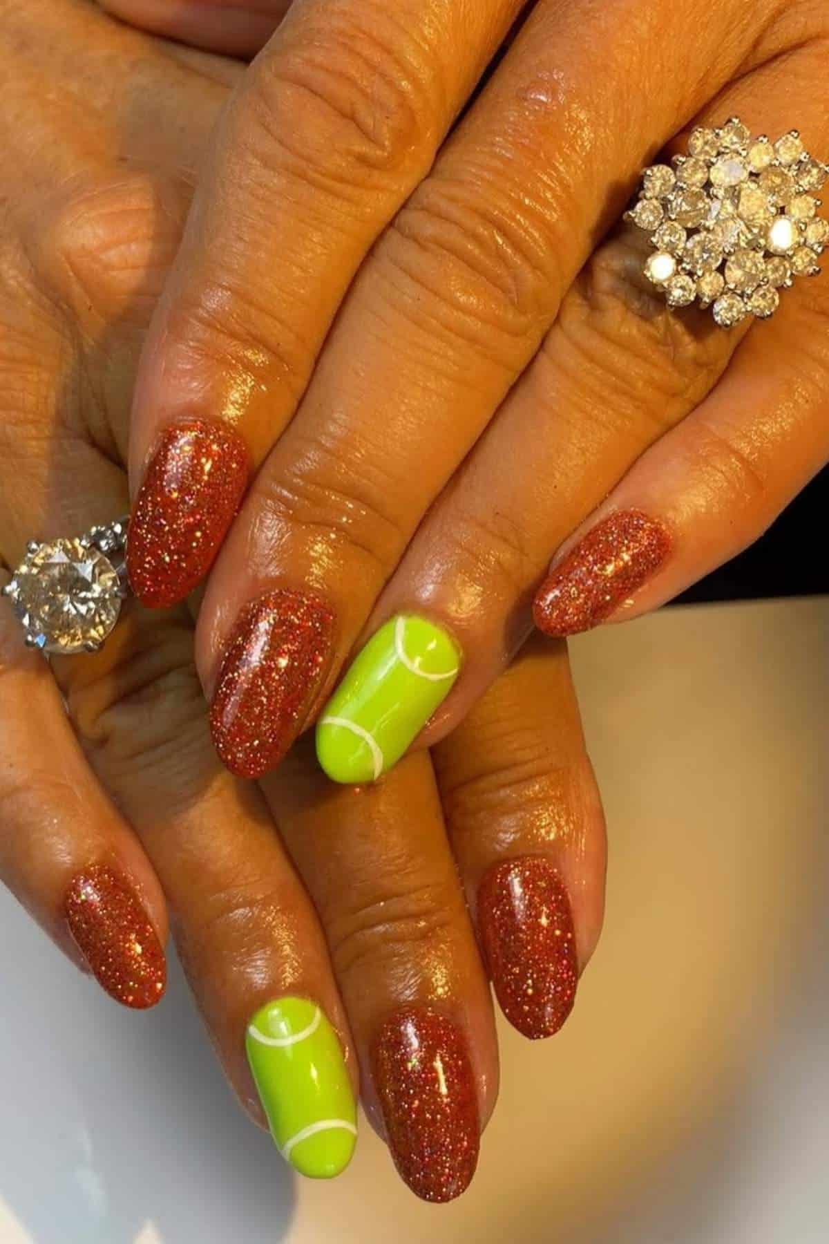 Close-up of hands with glittery red nails, two nails painted bright green with tennis ball designs, and diamond rings on two fingers.
