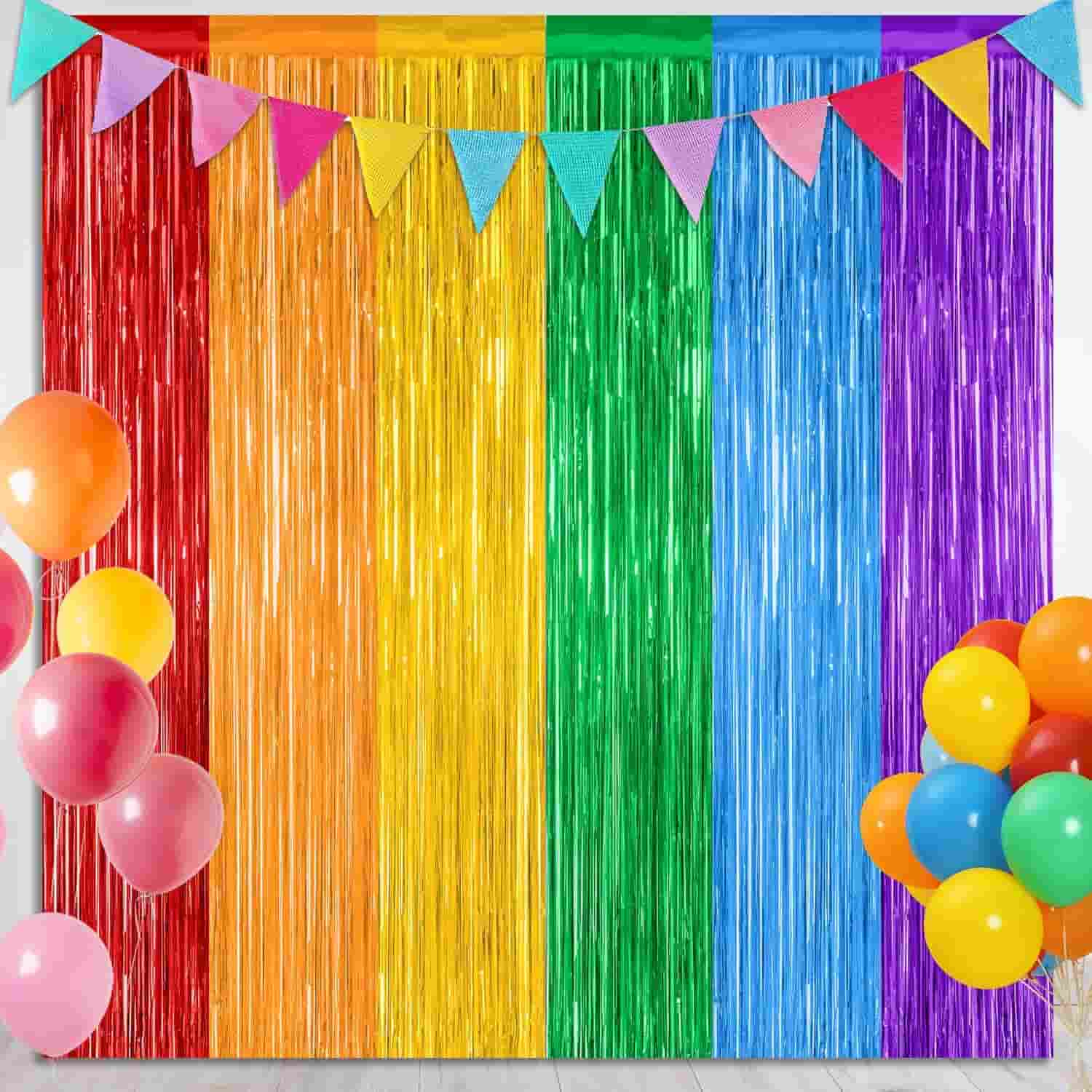 Rainbow-colored tinsel backdrop with multi-colored balloons and a string of triangle flags hanging above.
