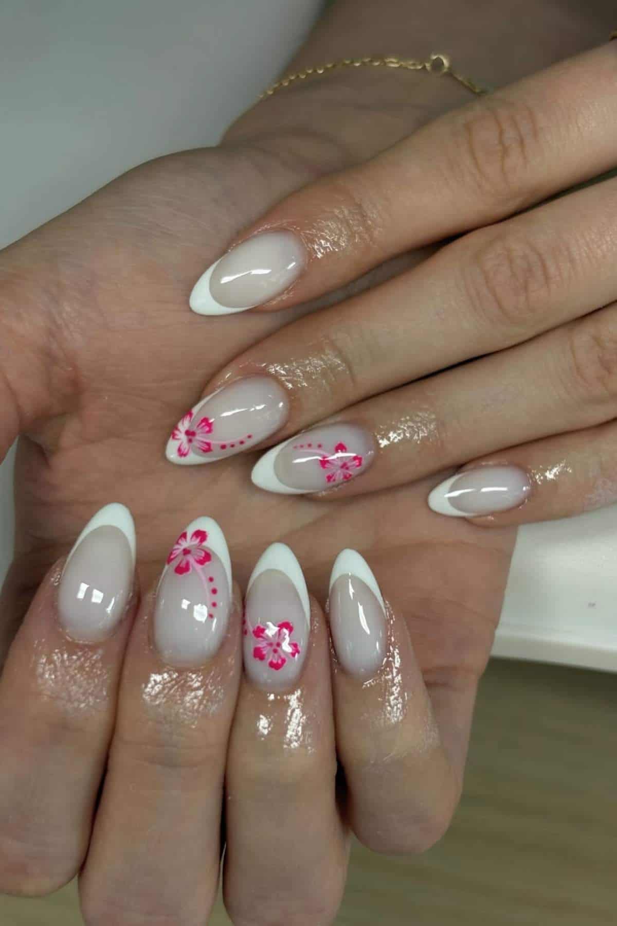 A hand with almond-shaped nails featuring a French manicure and pink floral designs on two nails.