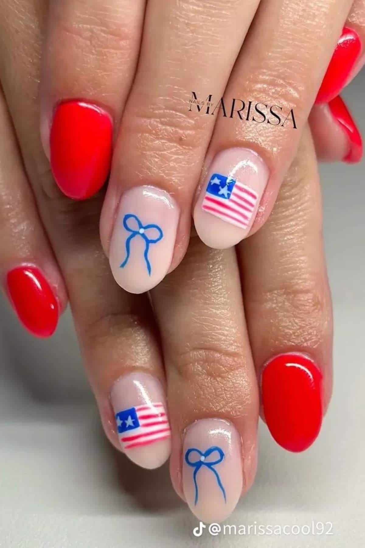 Hands with manicure featuring red nails; accent nails have a blue bow design and a stylized American flag on a nude base.