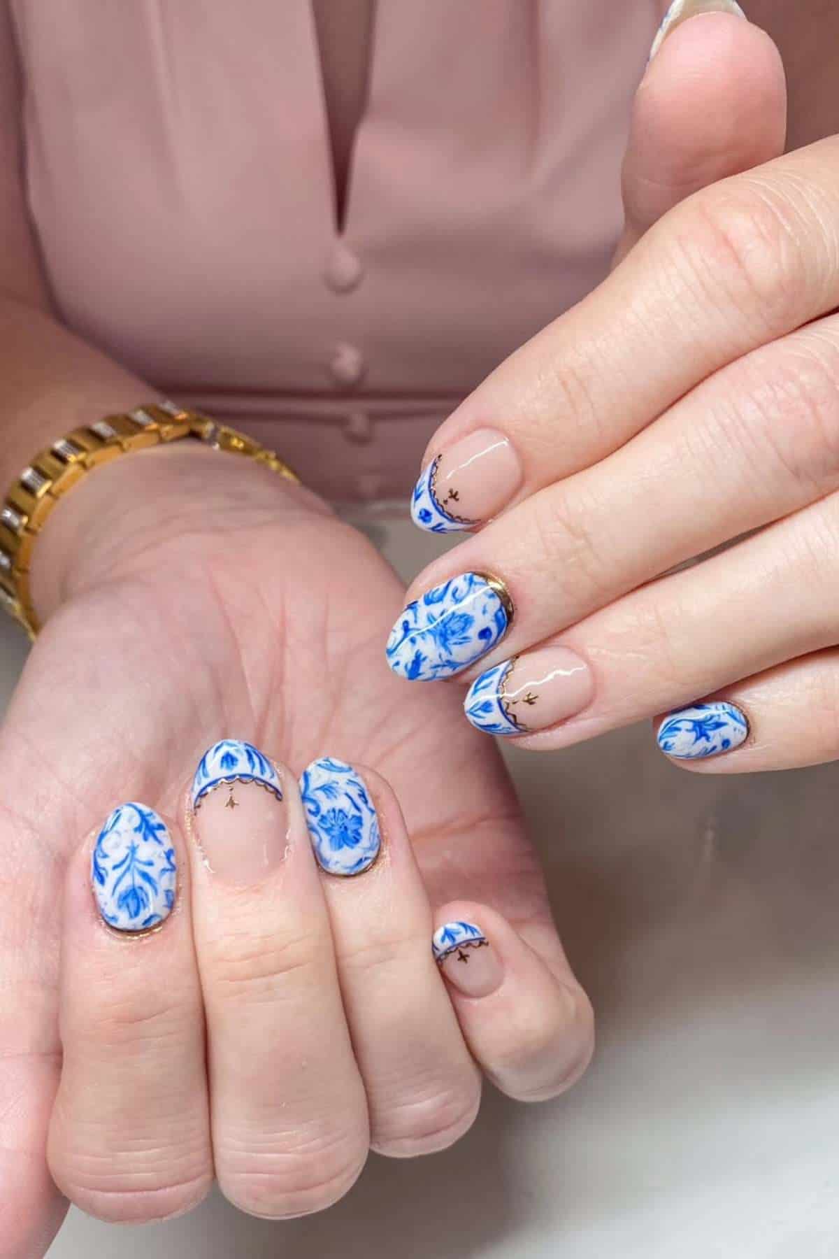Hands with blue and white floral patterned gel nail art, accent nails featuring nude polish and small gold star decals.