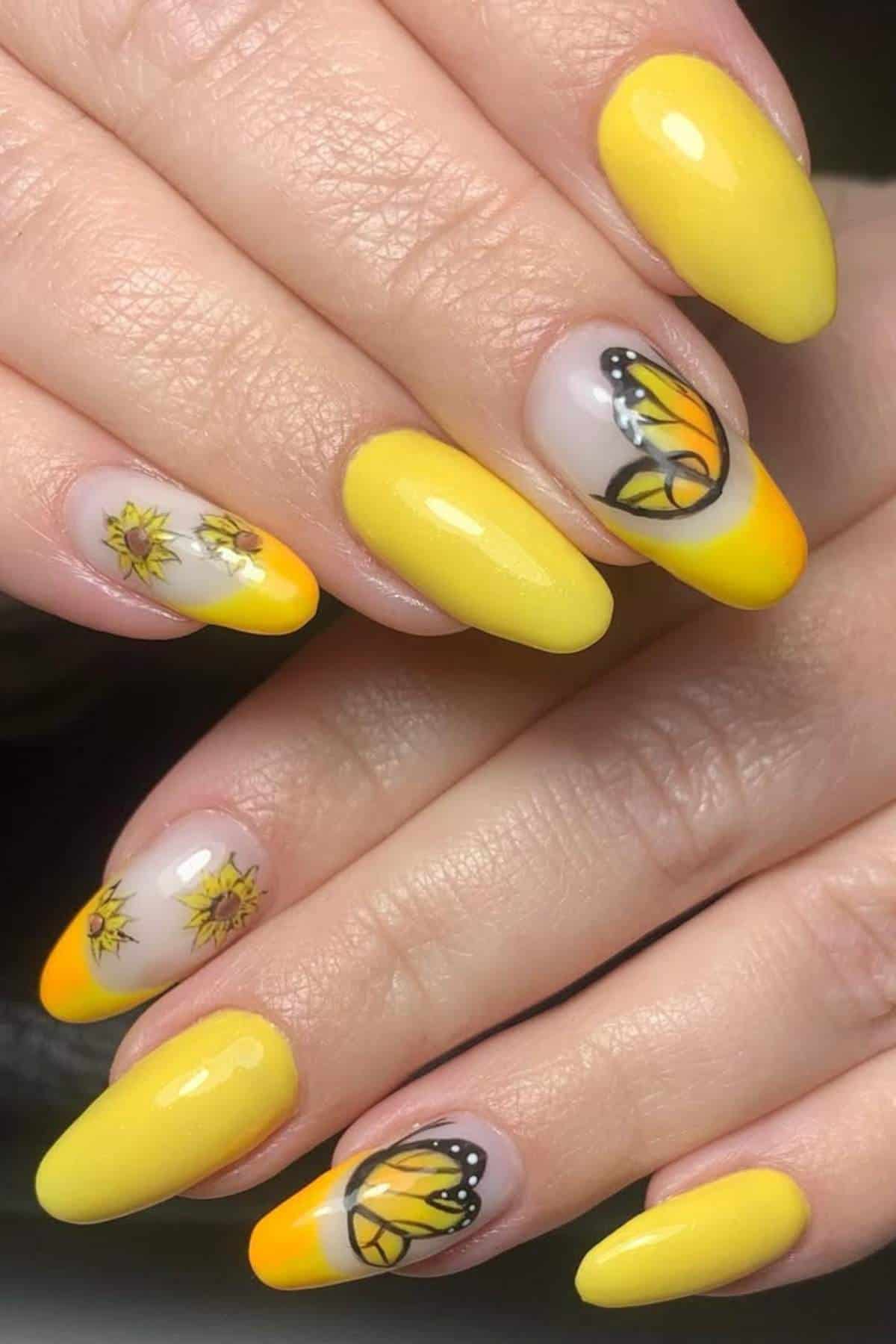 Hands with long yellow and orange gradient nails, featuring accent designs of butterflies and sunflowers on two nails.