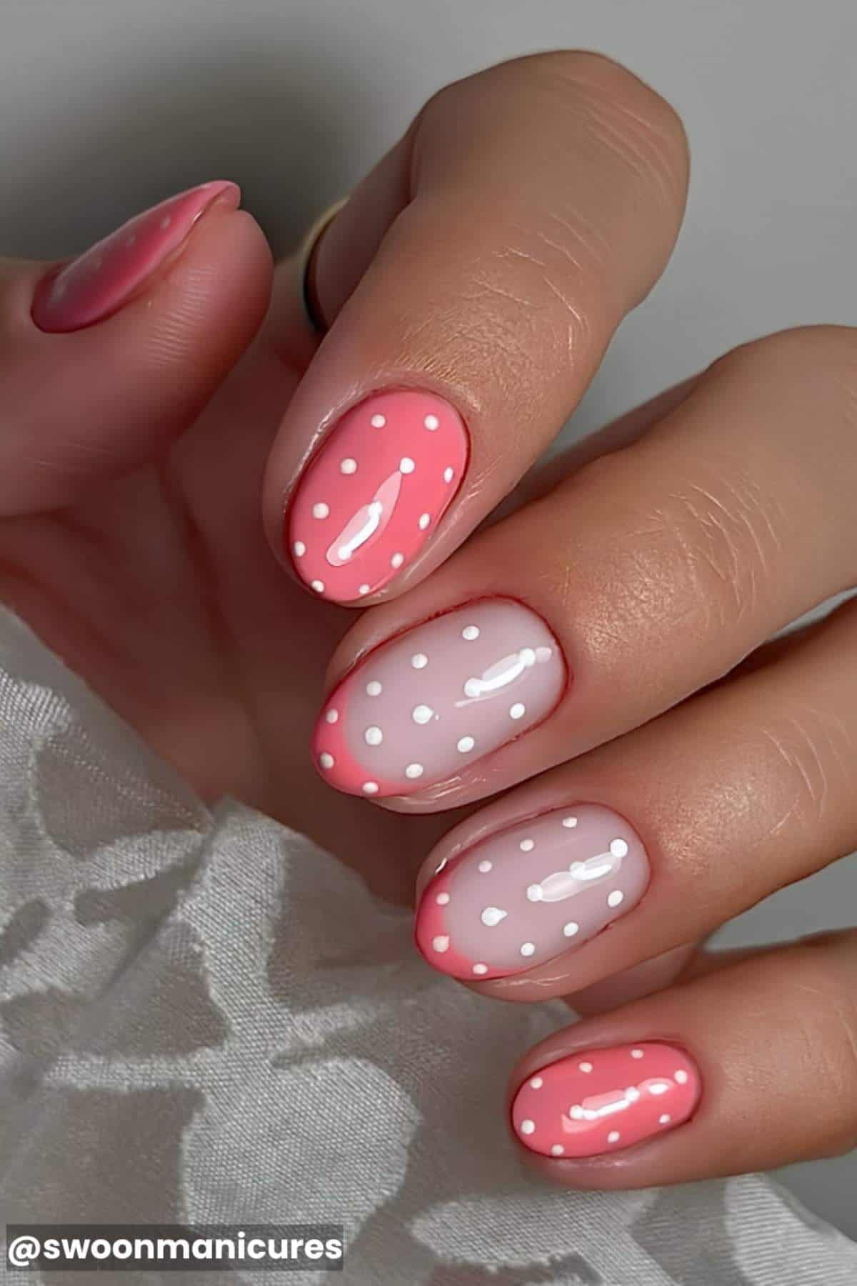 A hand with pink and nude nails featuring white polka dot nail art and a glossy finish.