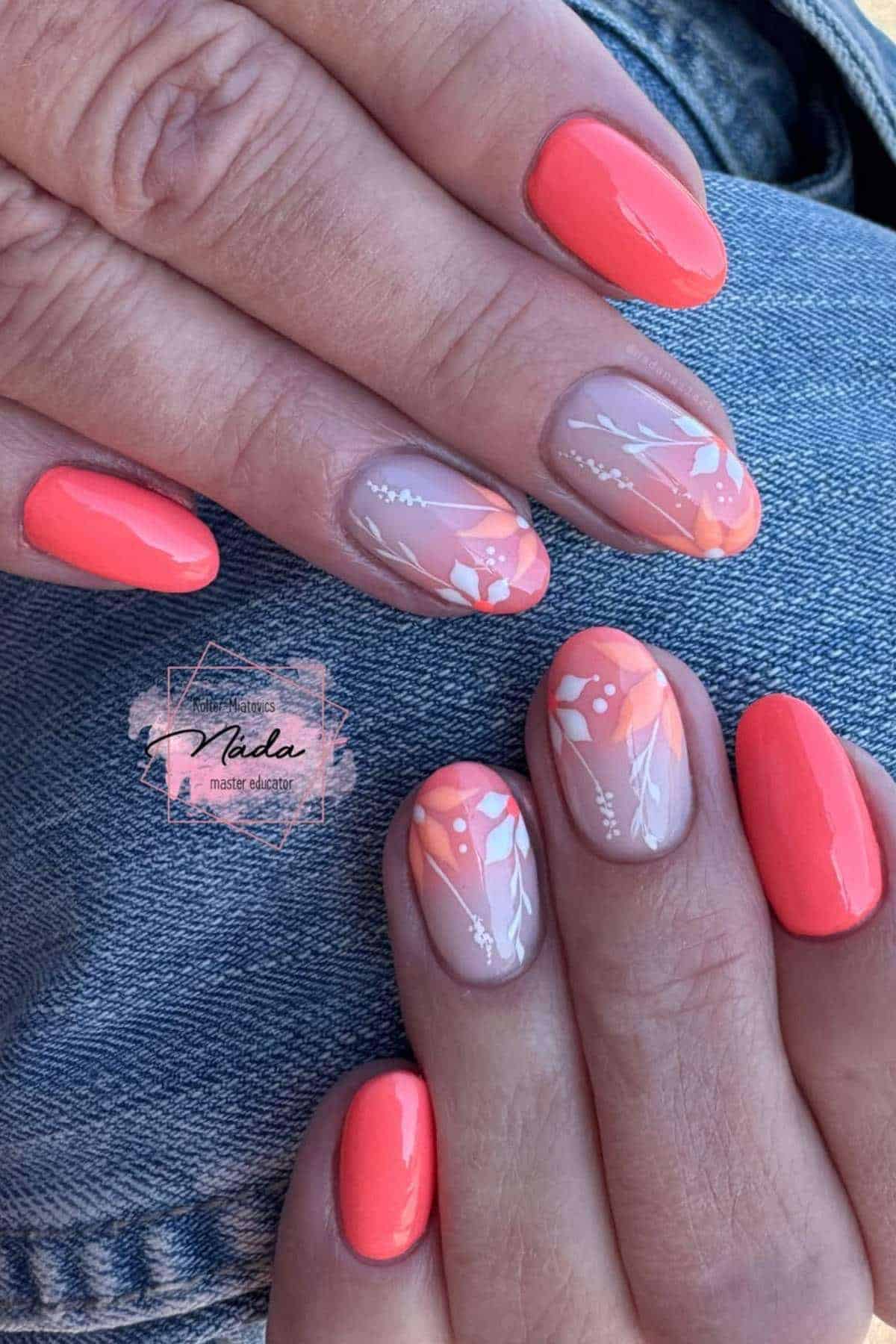 Hands with coral-colored manicure; some nails feature nude bases with orange tips and white floral designs. Hands rest on blue denim fabric.