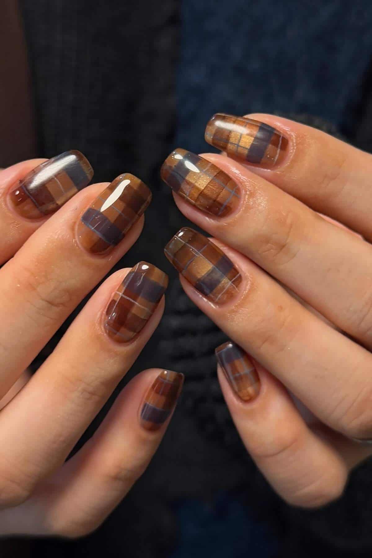 Close-up of hands showing fingernails with a glossy, brown and black geometric plaid pattern nail art design.