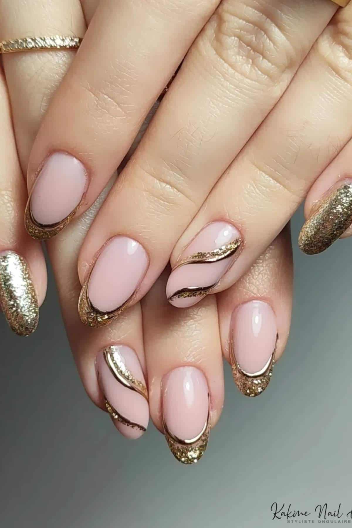 Close-up of hands with almond-shaped nails featuring a pink base, gold glitter French tips, and wavy gold accents on some nails.