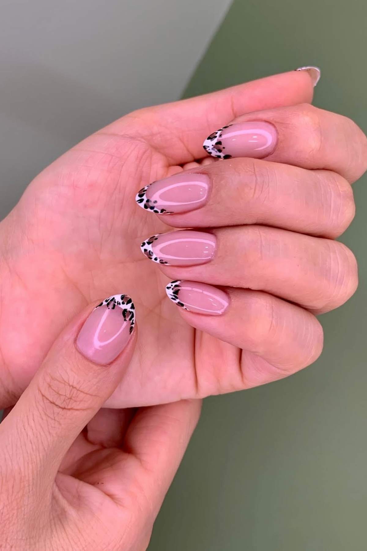 A hand with almond-shaped nails featuring a light pink base and black-and-white animal print tips.