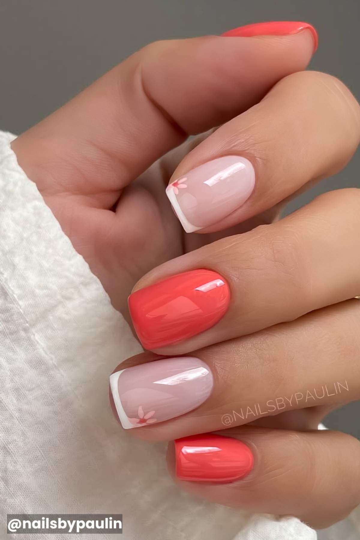 Close-up of a hand with manicured nails; two nails are painted coral, two are nude with white French tips and small pink floral accents.