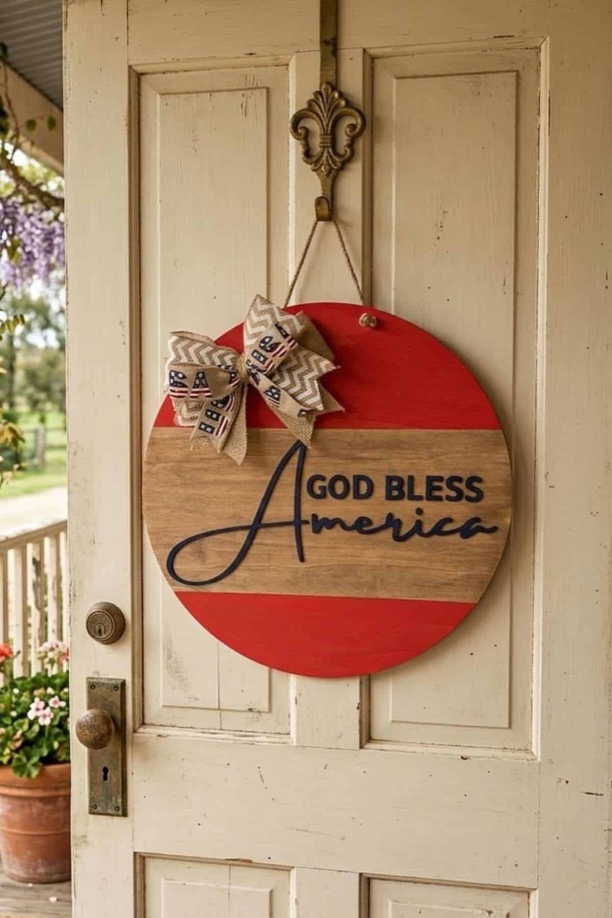 A round wooden sign with a red border and the words "God Bless America" hangs on a door, decorated with a bow featuring stars and "USA" text.