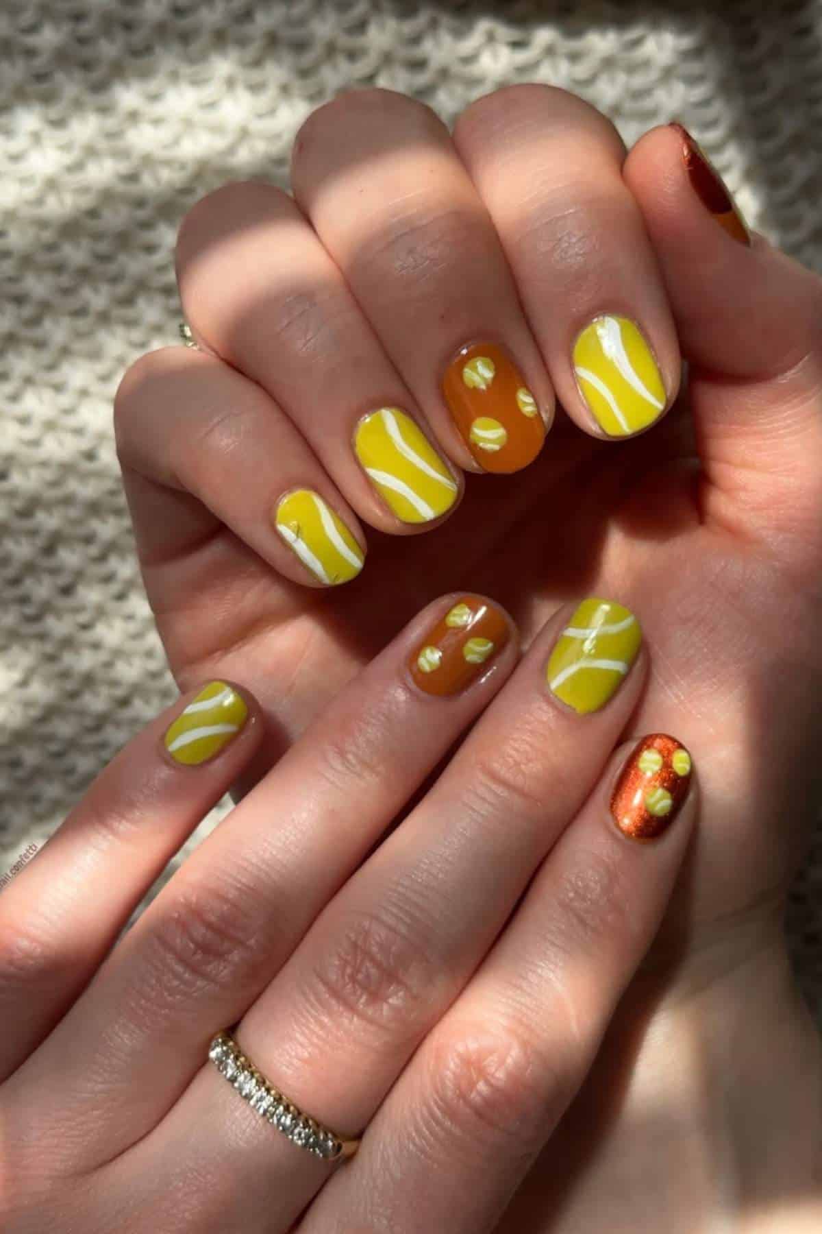 Hands with manicured nails featuring yellow and brown polish with abstract lines and dot designs, shown in natural sunlight.