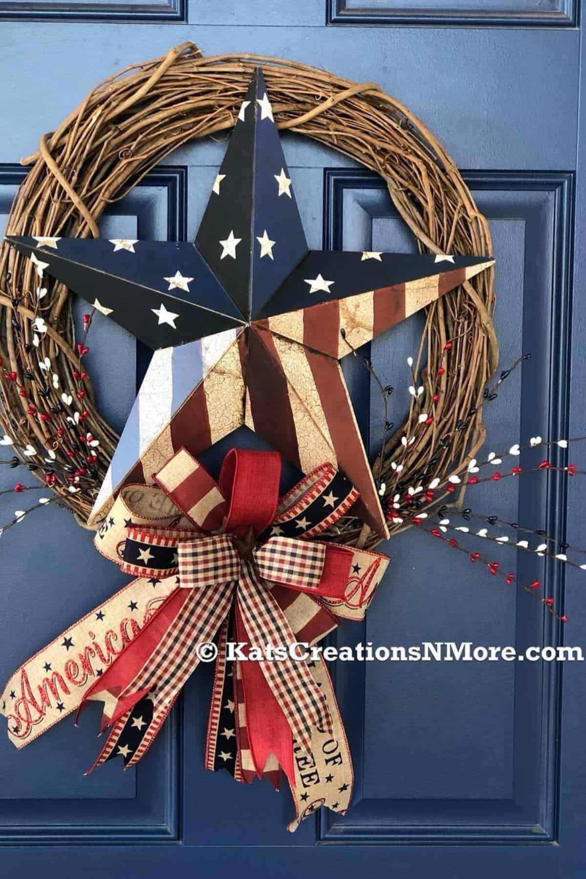A grapevine wreath with a large metal star painted in American flag colors, red and white berries, and a bow with "America" text on a blue door.