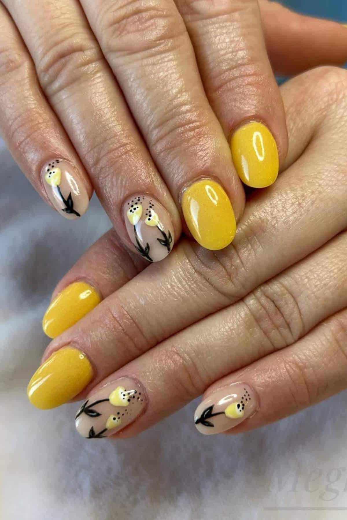 A hand with yellow and beige manicured nails; some nails feature black and yellow floral designs on a neutral background.