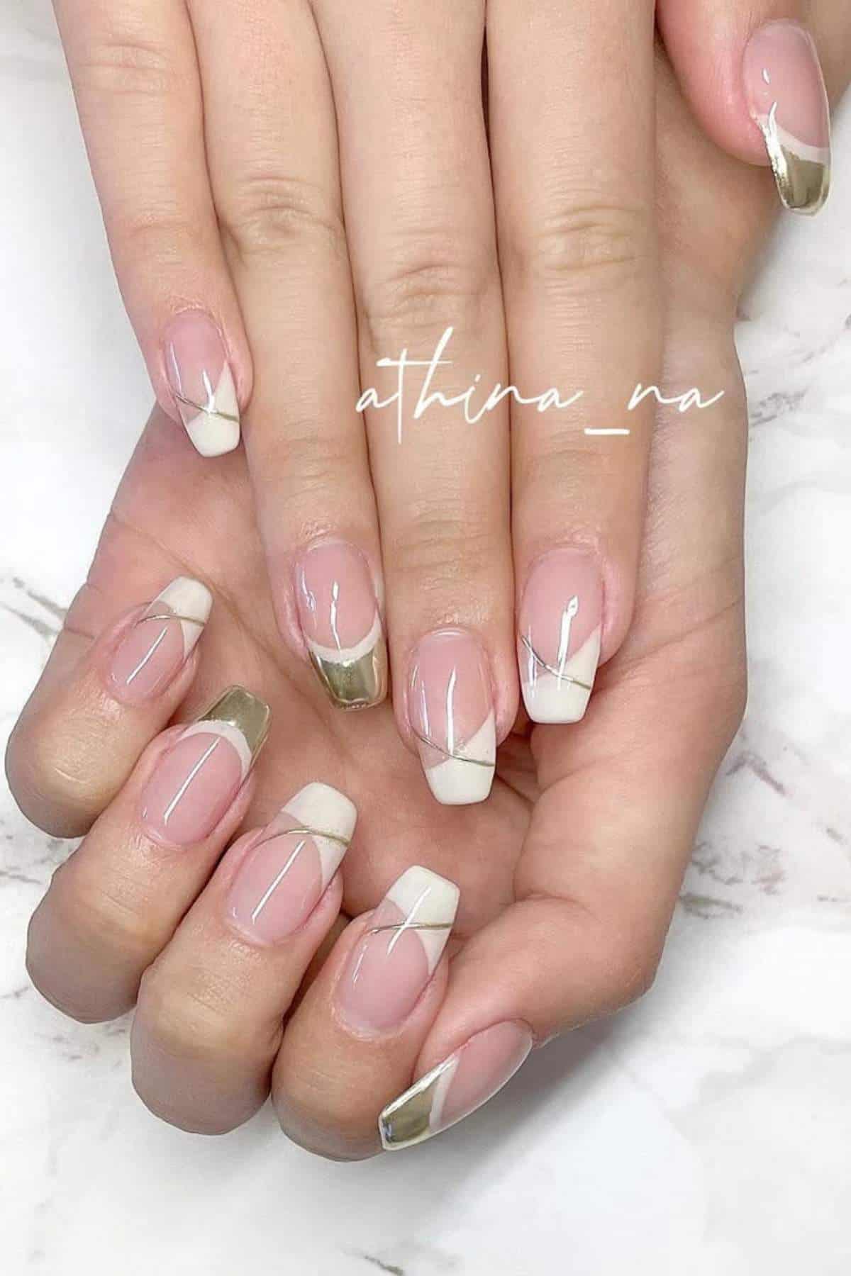 Hands with manicured nails featuring a minimalist design with white tips, gold accents, and thin white diagonal lines on a light pink base.