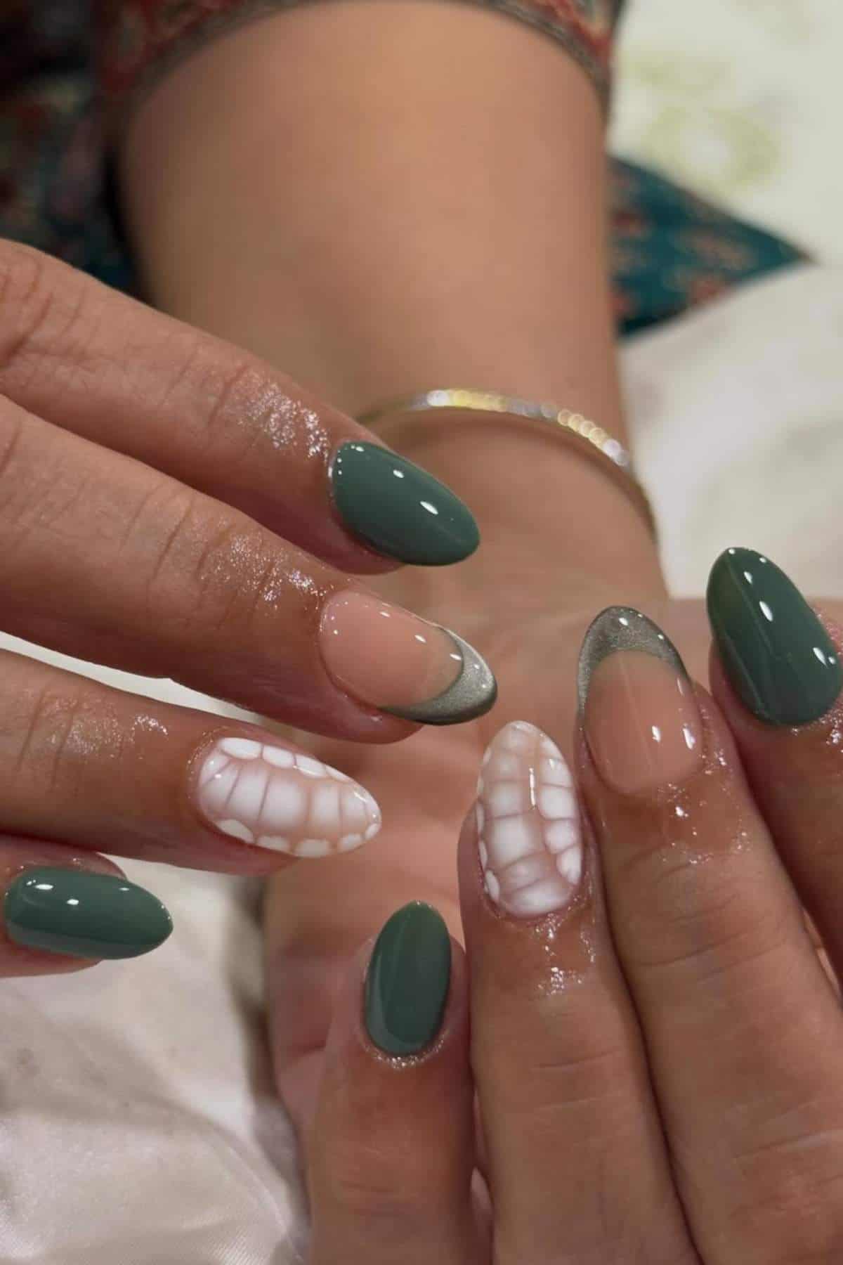 Close-up of hands with manicured nails featuring green, nude, silver tips, and white textured designs on a few nails.