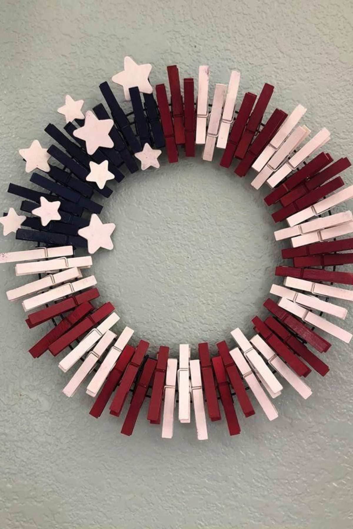 A circular wreath made of red, white, and blue clothespins with white star decorations, arranged to resemble the American flag.