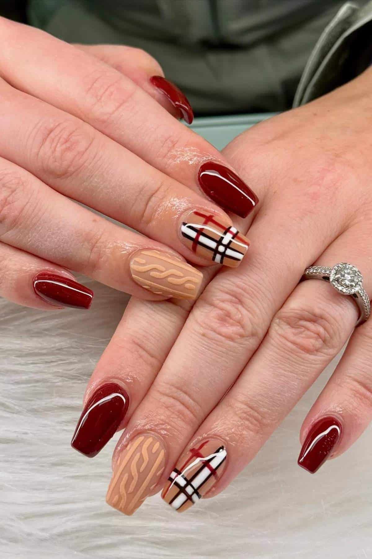 Hands with manicured nails featuring burgundy polish, plaid and wavy beige accent designs, and a diamond engagement ring on the left hand.