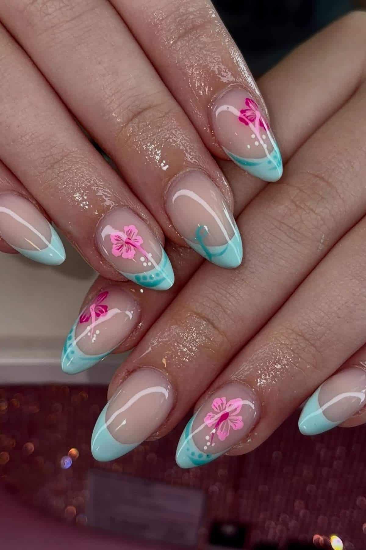 Hands with long, almond-shaped nails featuring light blue French tips and pink floral nail art designs with green accents.