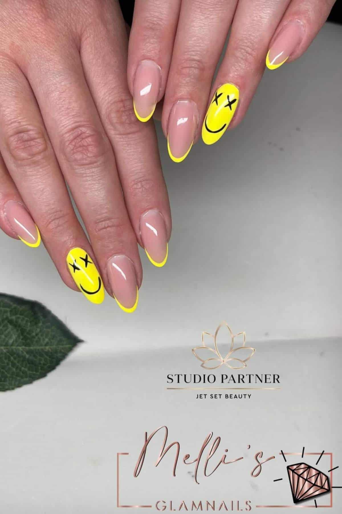 Hands with almond-shaped nails featuring neon yellow French tips; two accent nails have yellow smiley faces, one with X's for eyes.