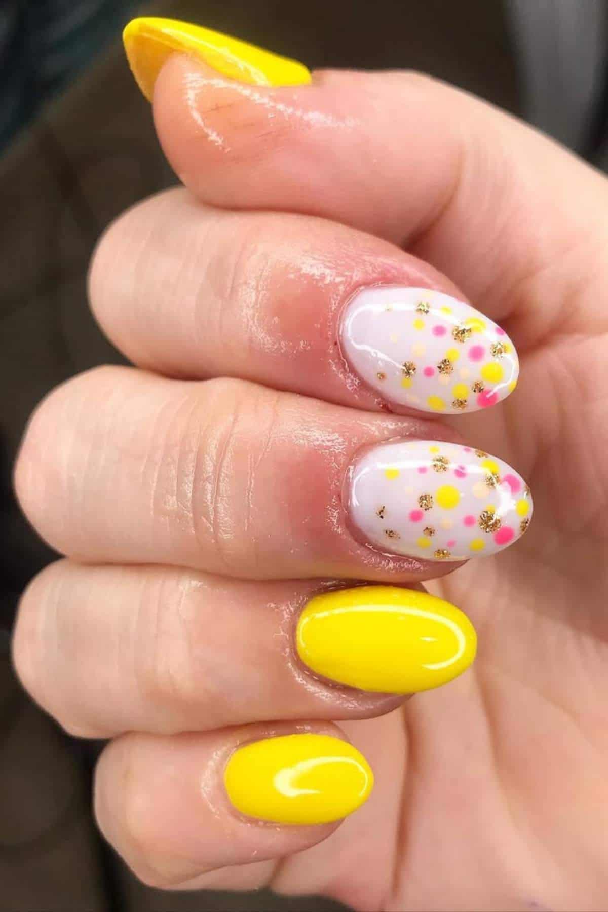 A hand with yellow painted nails; two nails have a white base with small yellow and pink flower designs.