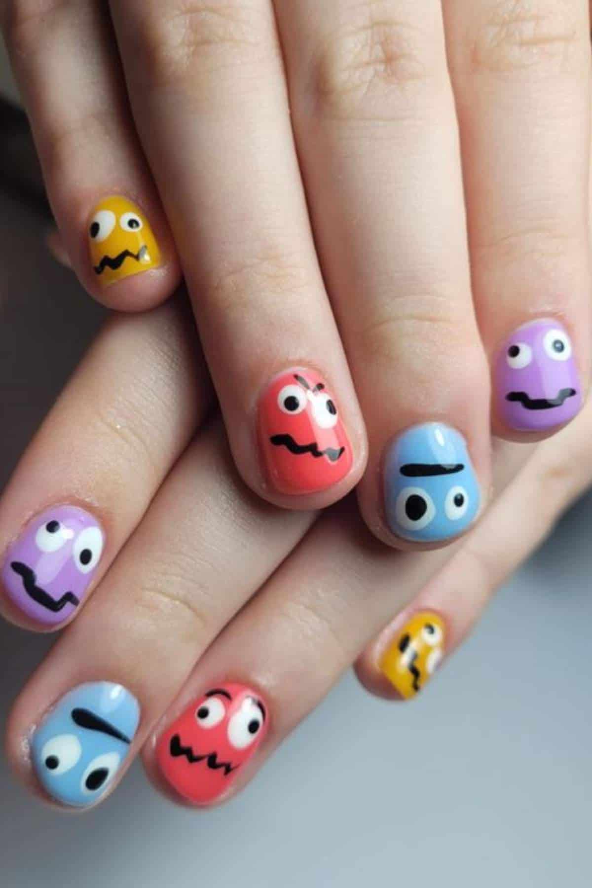 Fingernails painted with colorful cartoon faces, each with wide eyes and wavy mouths, on a variety of pastel backgrounds.