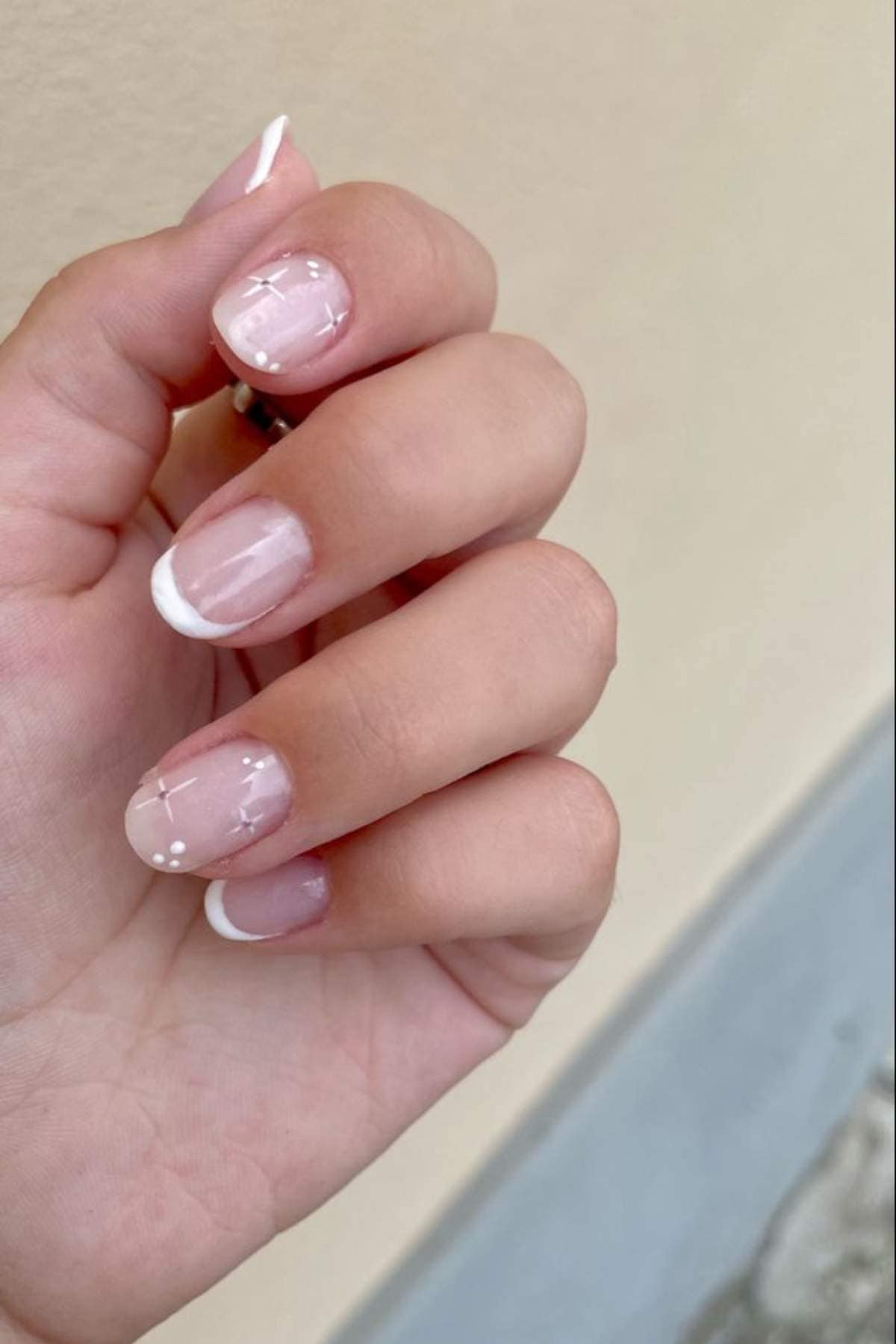A hand with short, natural nails featuring a French manicure with white tips and small white dot accents on a couple of nails.