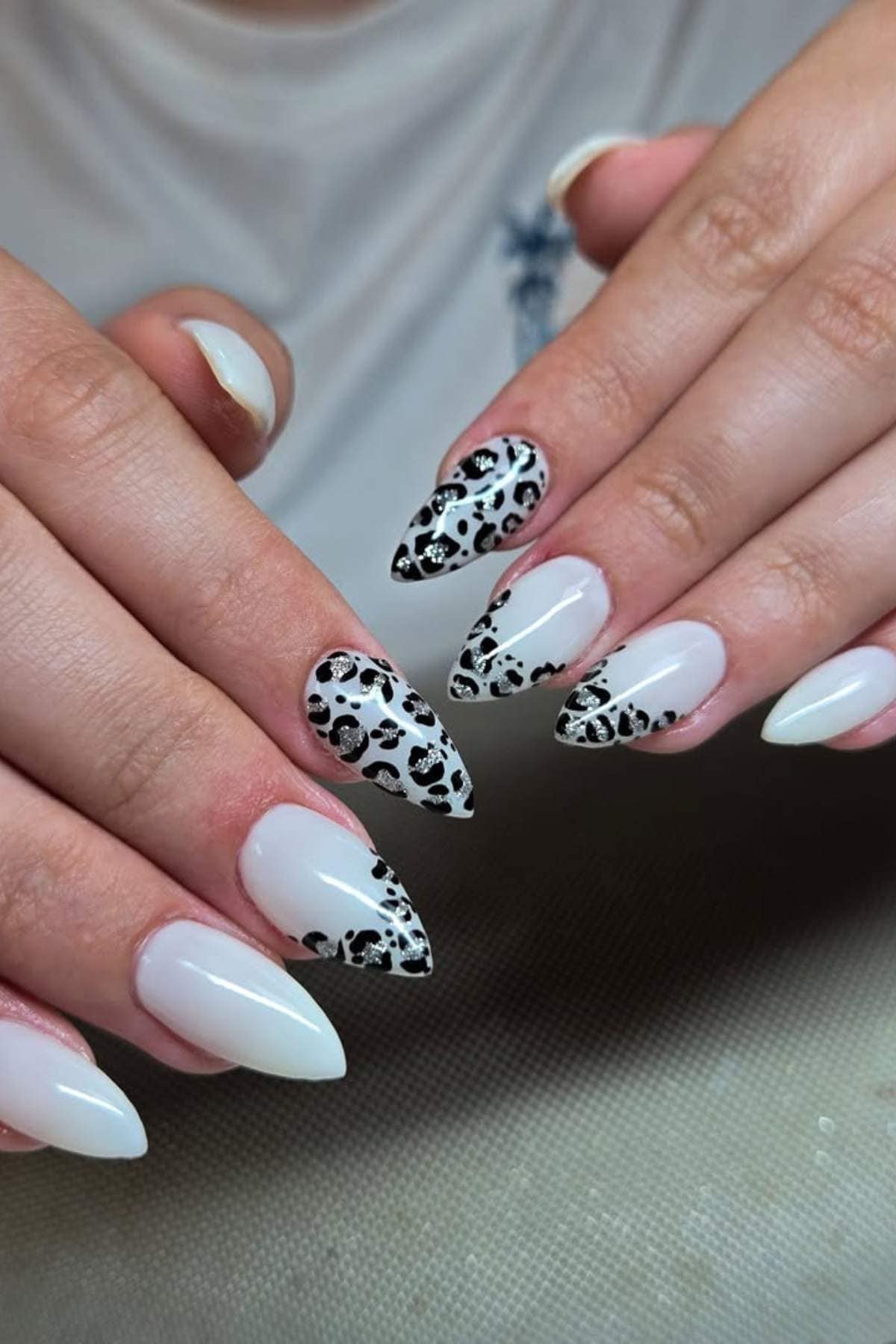 A person with long, almond-shaped acrylic nails painted white, featuring black and white animal print accent nails on each hand.