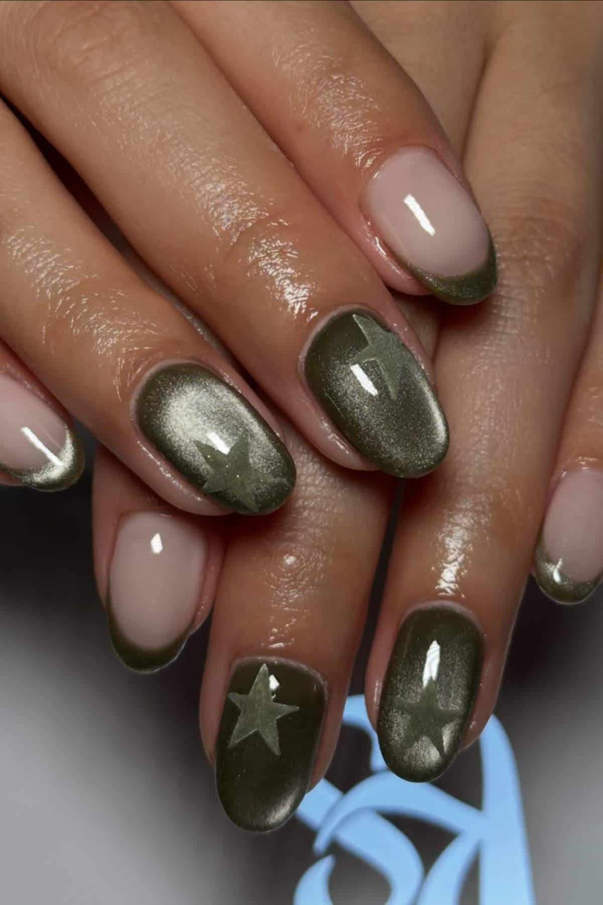 Close-up of hands with manicured nails; some nails are painted olive green with star designs, while others are nude with a green French tip.