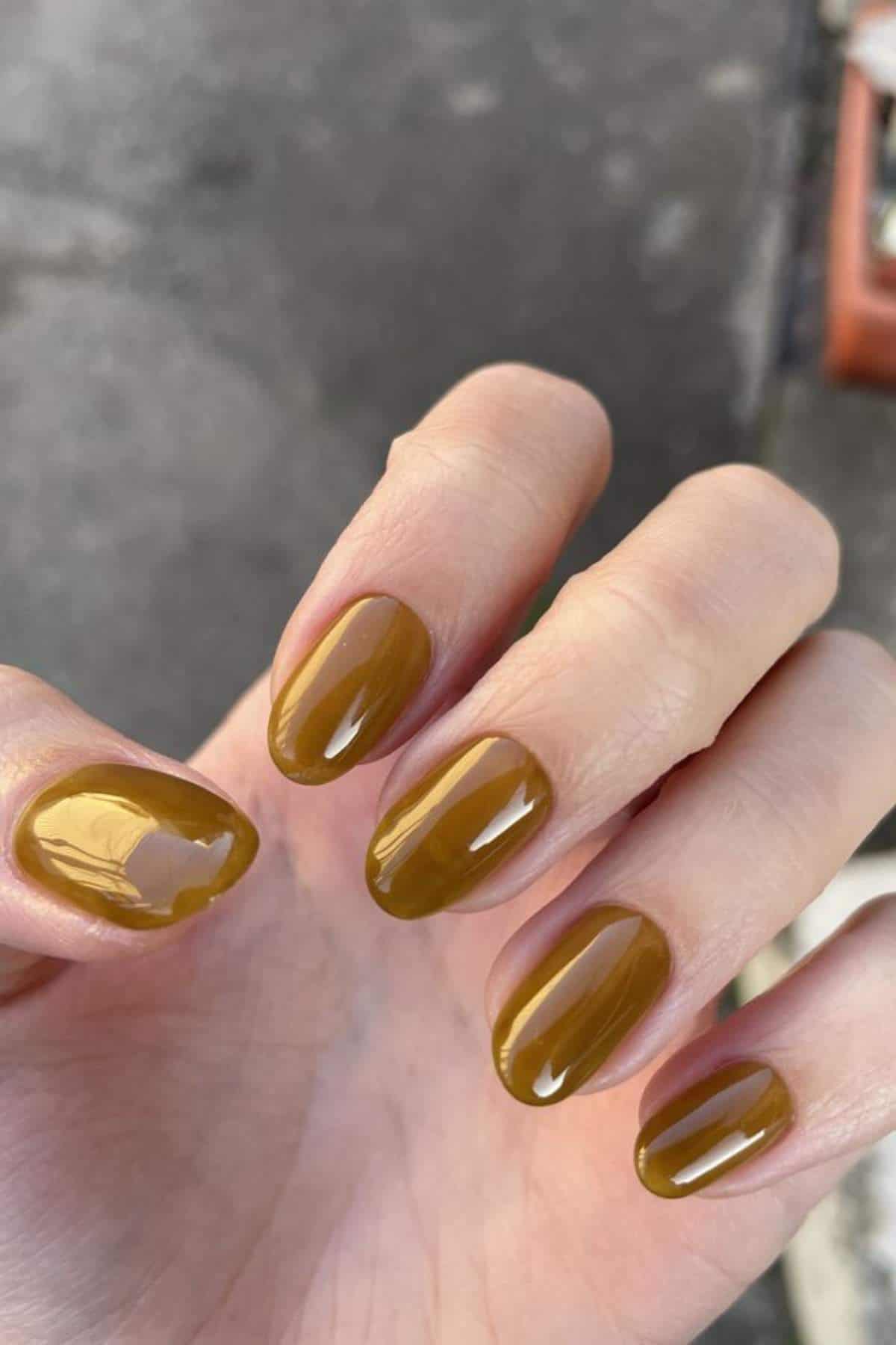A hand with short, rounded nails painted in glossy mustard yellow polish; the polish on the thumb is chipped.