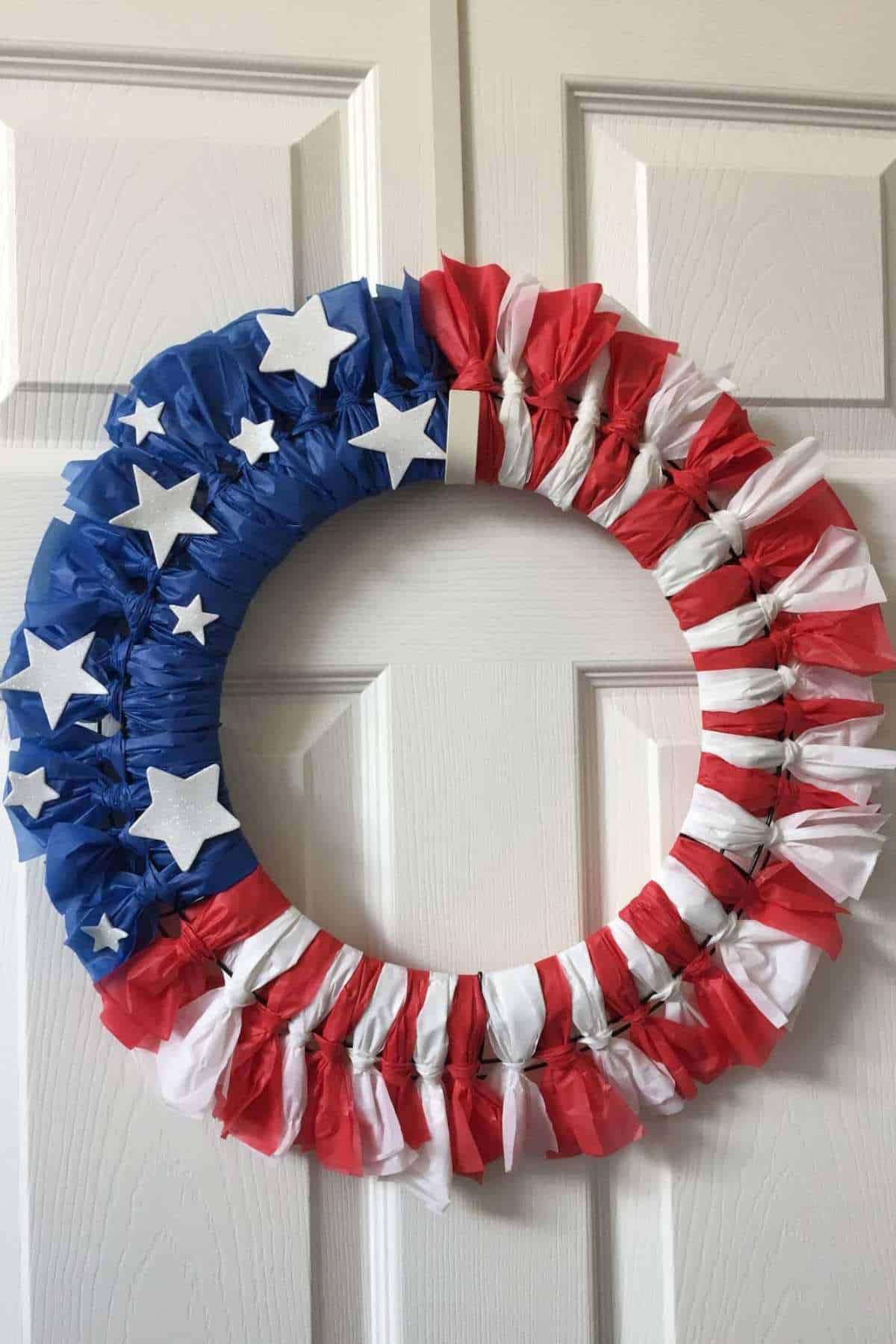 A patriotic wreath decorated with blue, red, and white sections and white stars, resembling the American flag, hanging on a white paneled door.