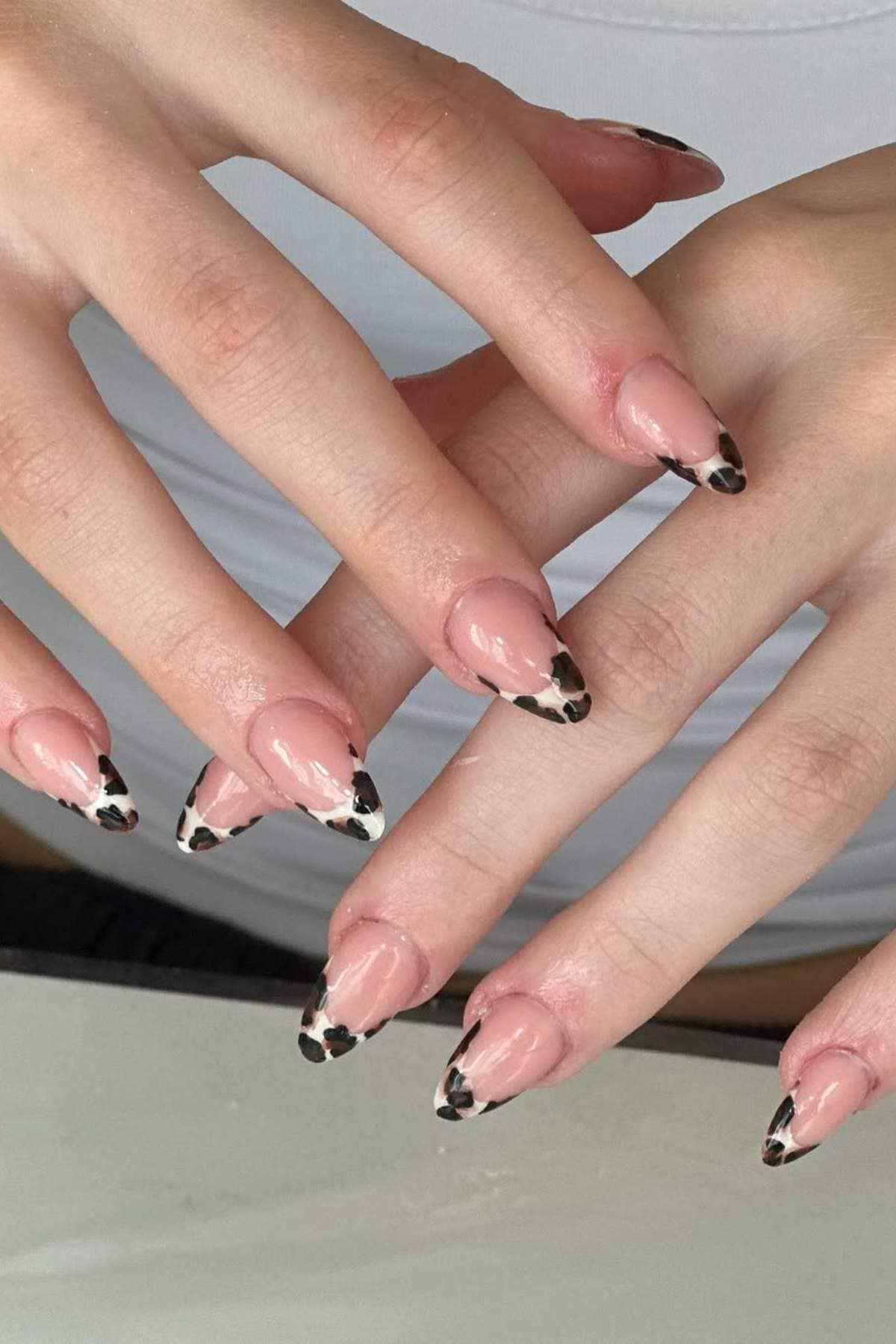 Hands with almond-shaped nails featuring a nude base and black and white animal print tips, resting on a white surface.