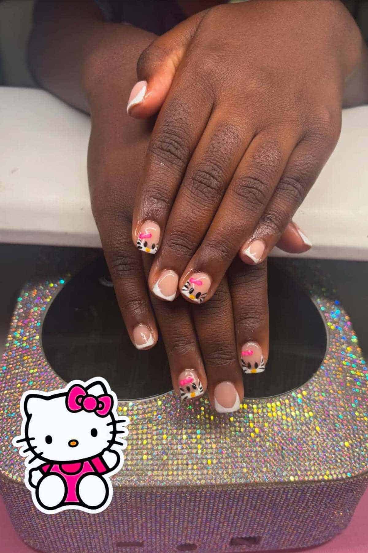 Hands with a fresh manicure featuring pink, black, and white floral nail art on a sparkly surface, with a Hello Kitty sticker in the corner.