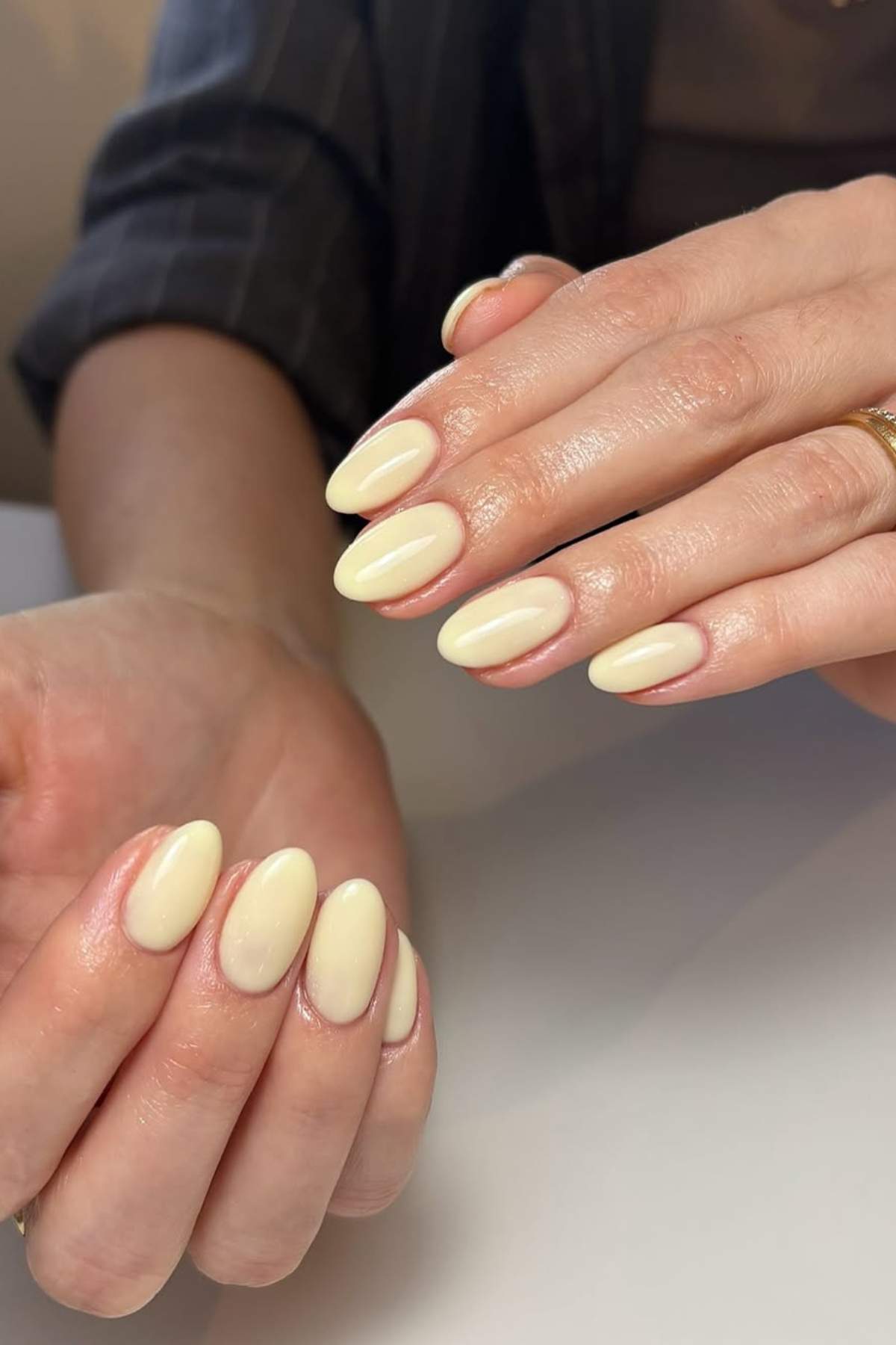 Hands with medium-length, almond-shaped nails painted in a glossy pale yellow polish.
