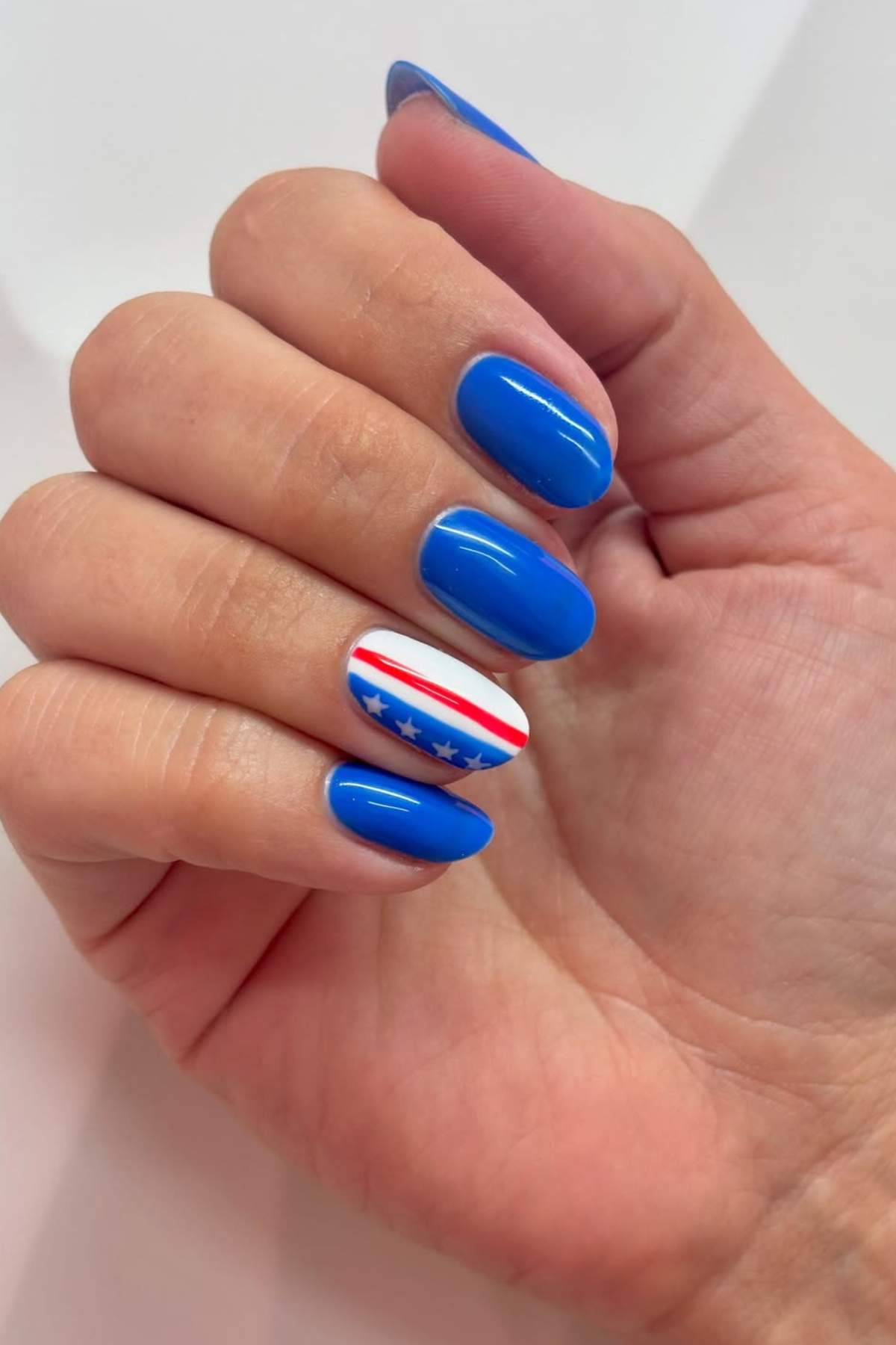 A hand with blue painted fingernails; the ring fingernail features a design with red stripes, blue stars, and a white background.