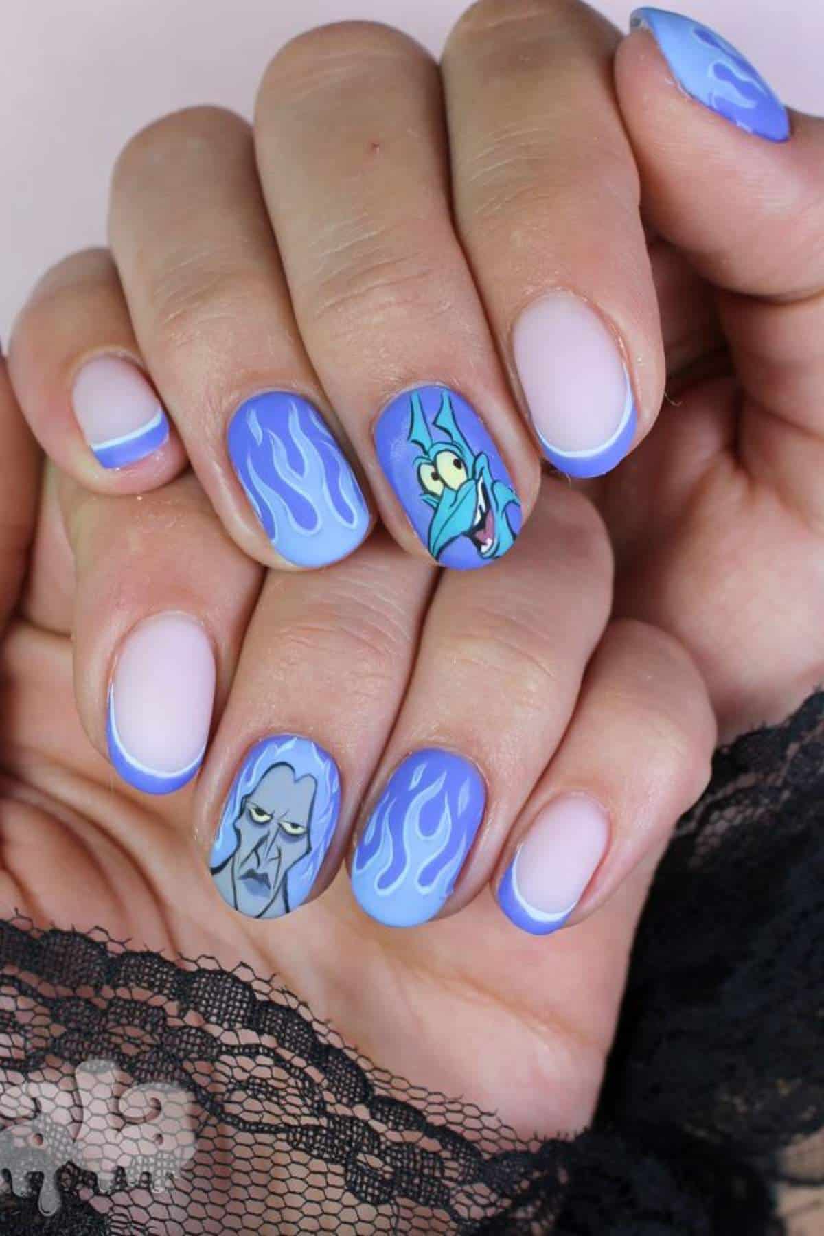 Close-up of hands with blue and white French tip nails, featuring cartoon character faces and blue flame designs on two accent nails.