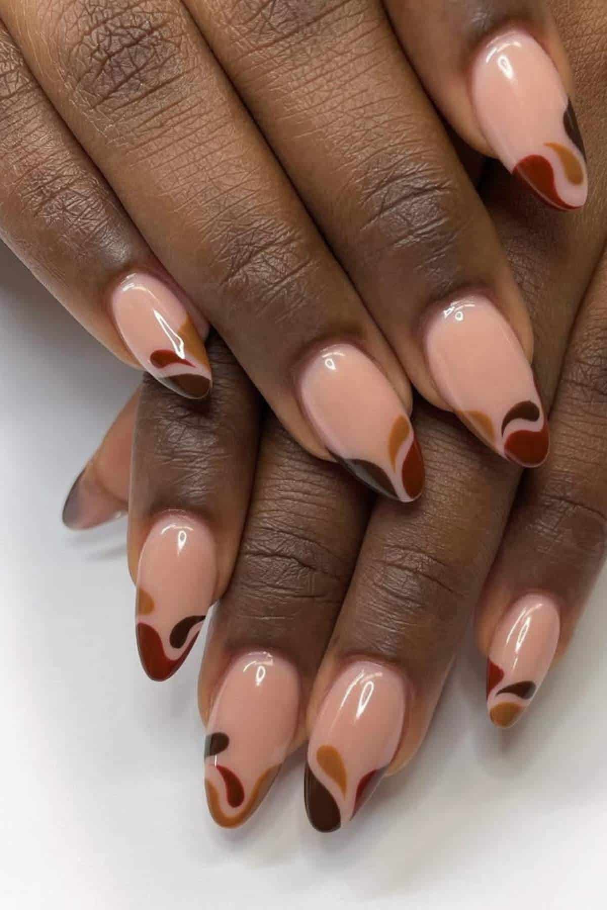Hands with almond-shaped nails featuring a nude base and abstract brown, rust, and dark red swirl designs on each nail.