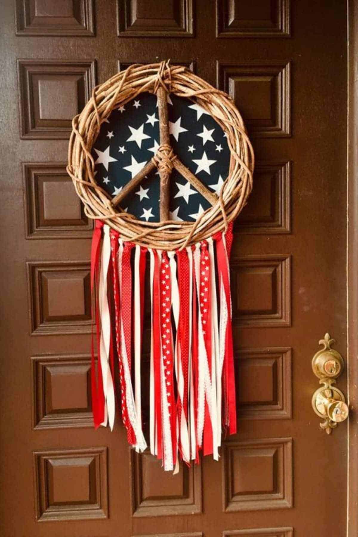 A patriotic wreath shaped like a peace sign with a background of white stars on blue and red, white, and patterned ribbons hanging below, displayed on a brown door.