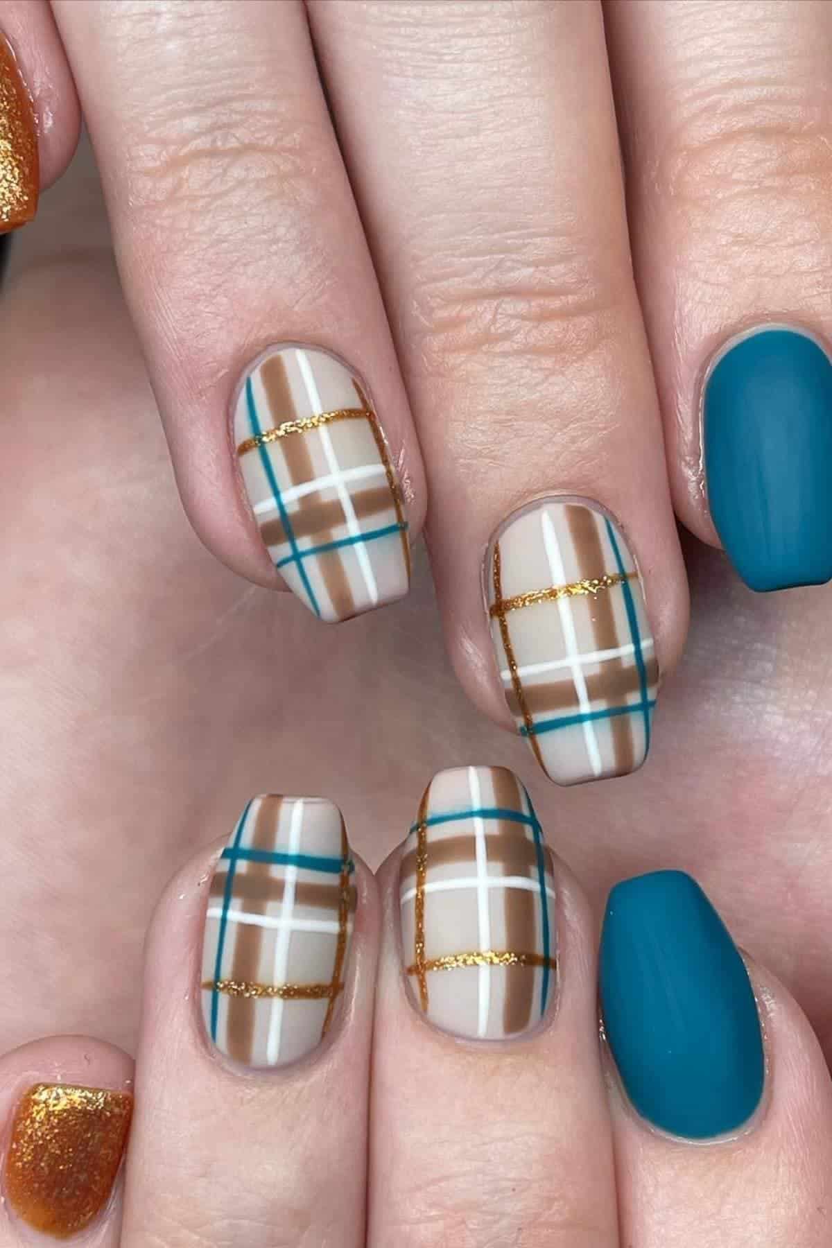 Close-up of hands with manicured nails featuring teal, gold glitter, and plaid designs in white, brown, blue, and gold lines.