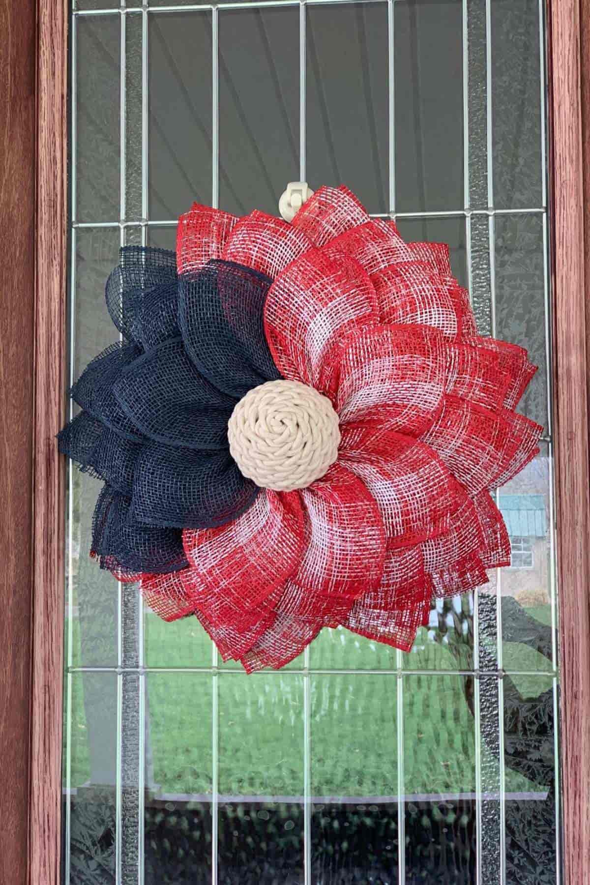A decorative wreath shaped like a flower with red, black, and beige petals hangs on a glass-paneled door.