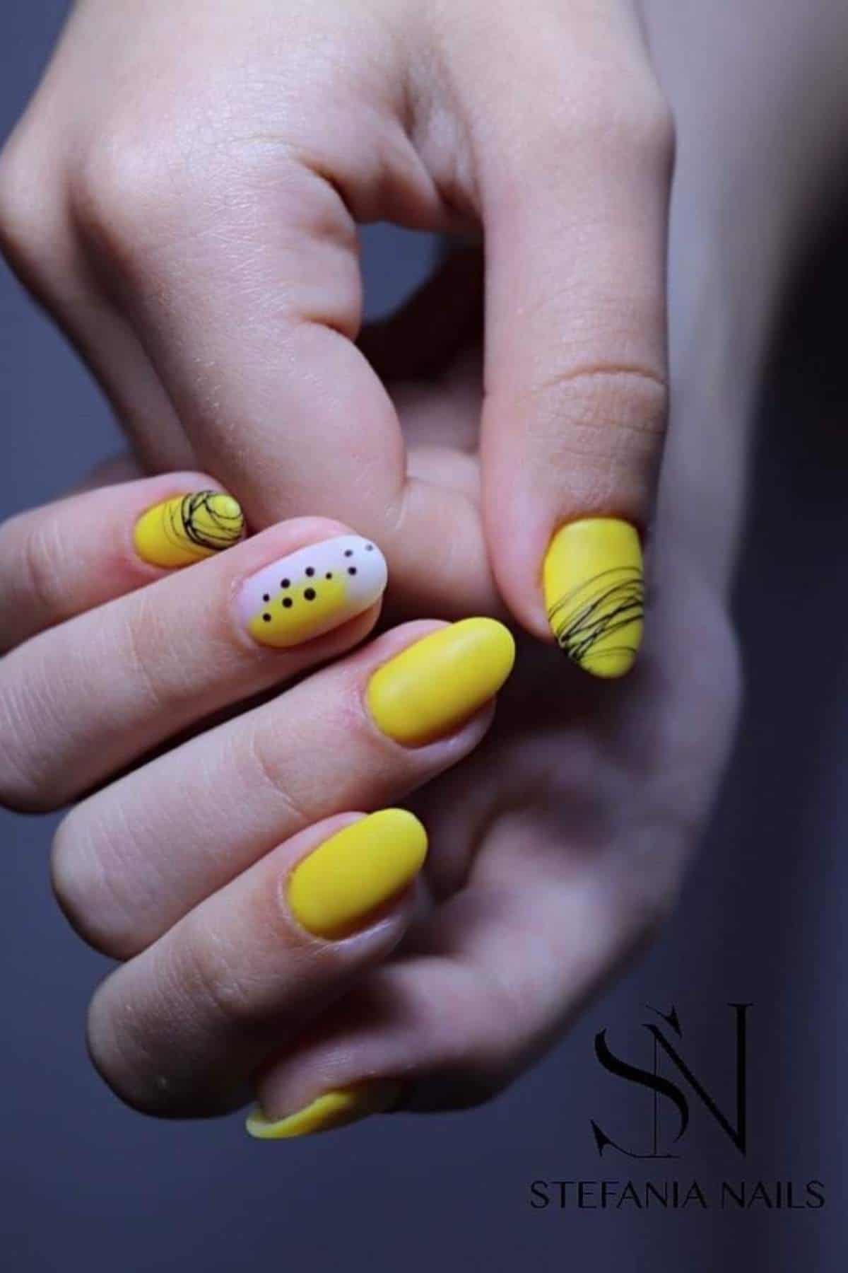Close-up of hands with yellow matte nail polish; accent nails feature black lines and dots on a light base. Logo at bottom reads "STEFANIA NAILS.