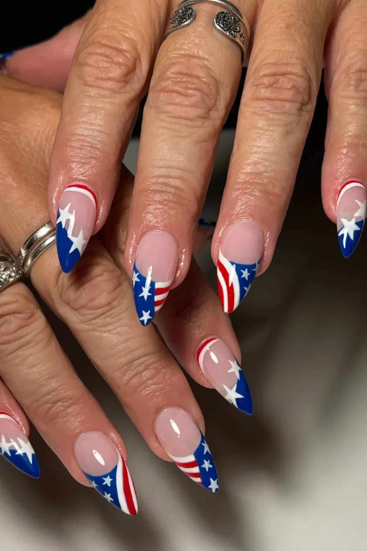 Hands with long, almond-shaped nails featuring a red, white, and blue American flag design with stars and stripes.