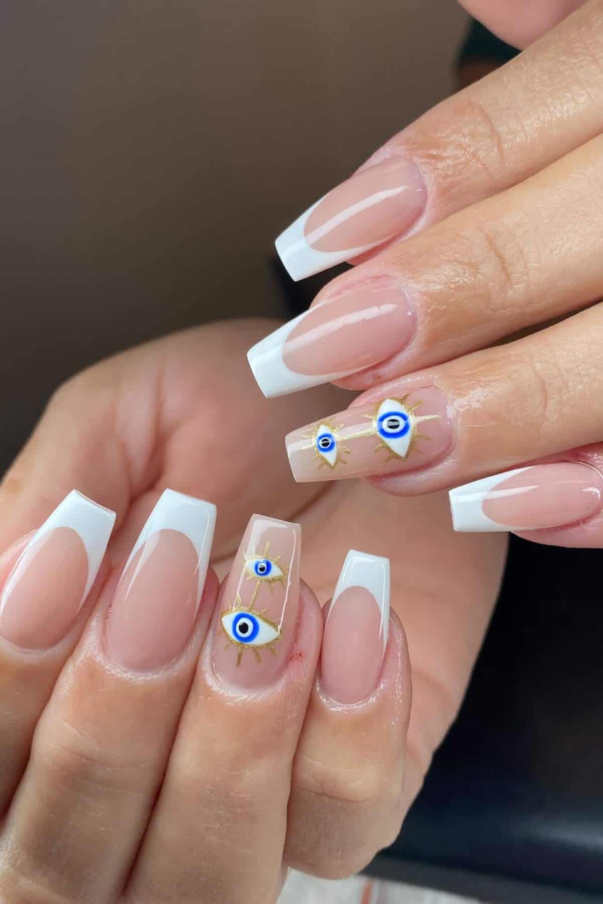 Hands with long, coffin-shaped French tip nails; ring and middle fingers feature gold accents and blue evil eye designs.