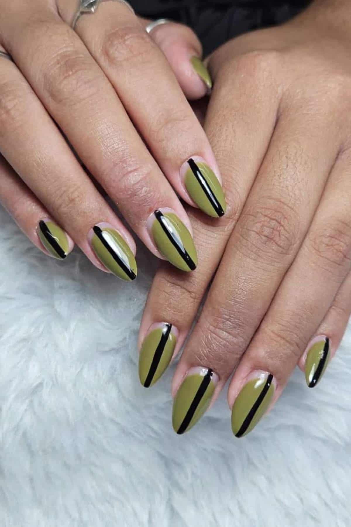 Hands with almond-shaped nails painted olive green, each nail featuring a single black vertical stripe down the center.