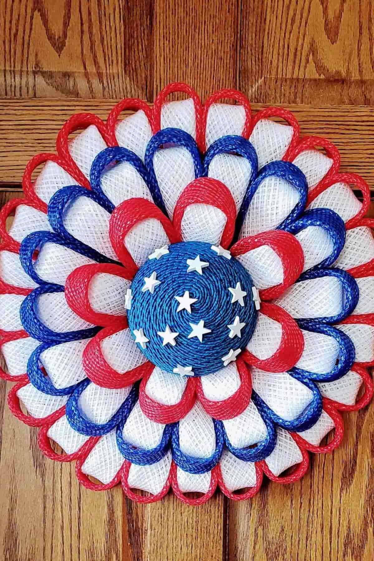 Patriotic wreath with red, white, and blue ribbon loops and a blue center with white stars, displayed on a wooden door.