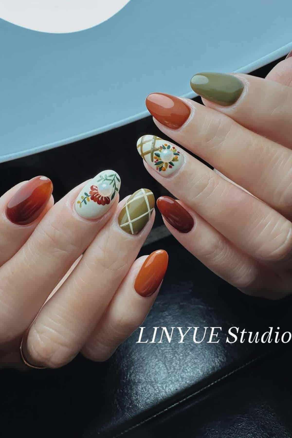 Hands with almond-shaped nails painted in autumn colors, featuring floral and plaid designs on some nails. "LINYUE Studio" text is visible.