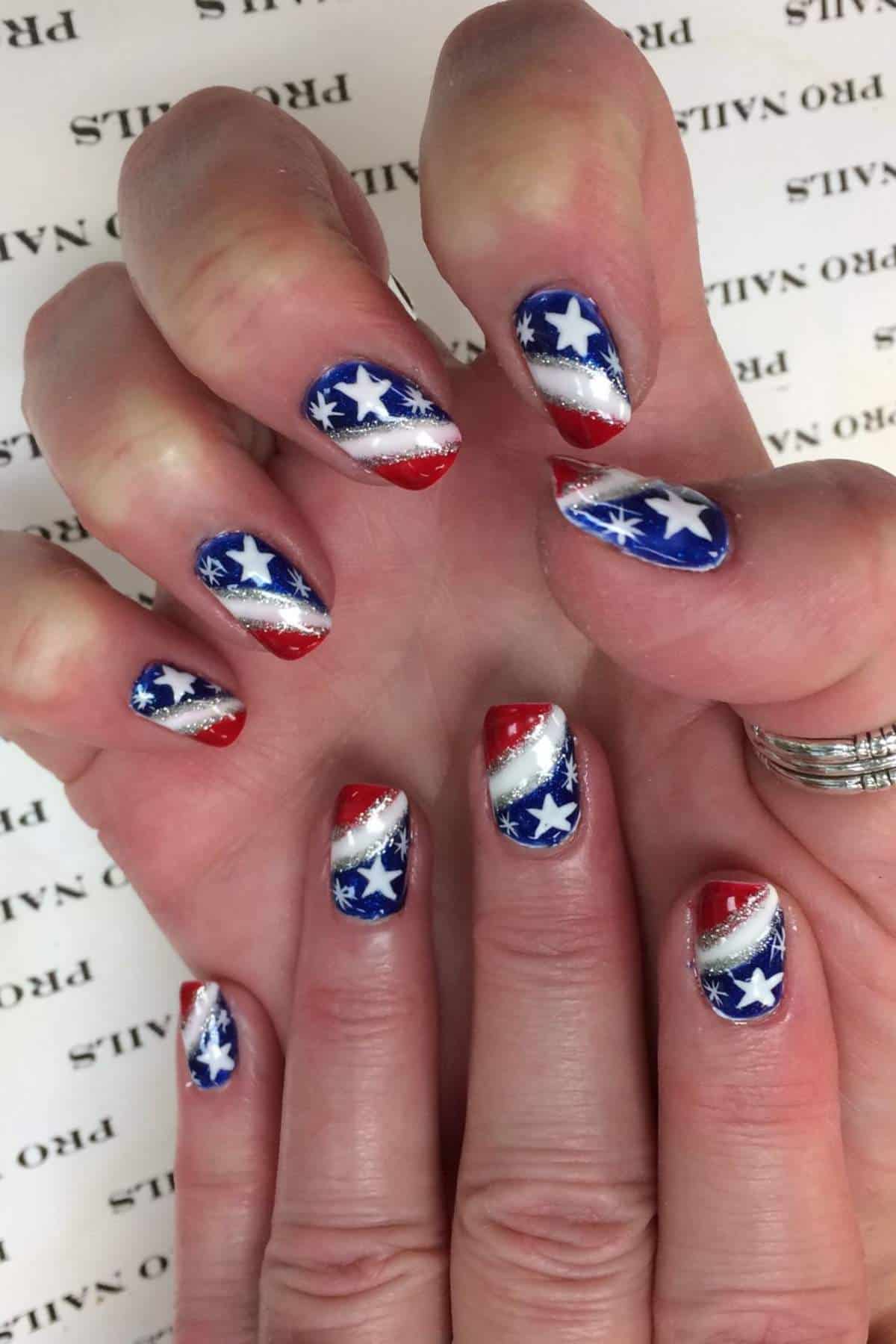 Fingernails painted with a red, white, and blue patriotic design featuring white stars and silver stripes.