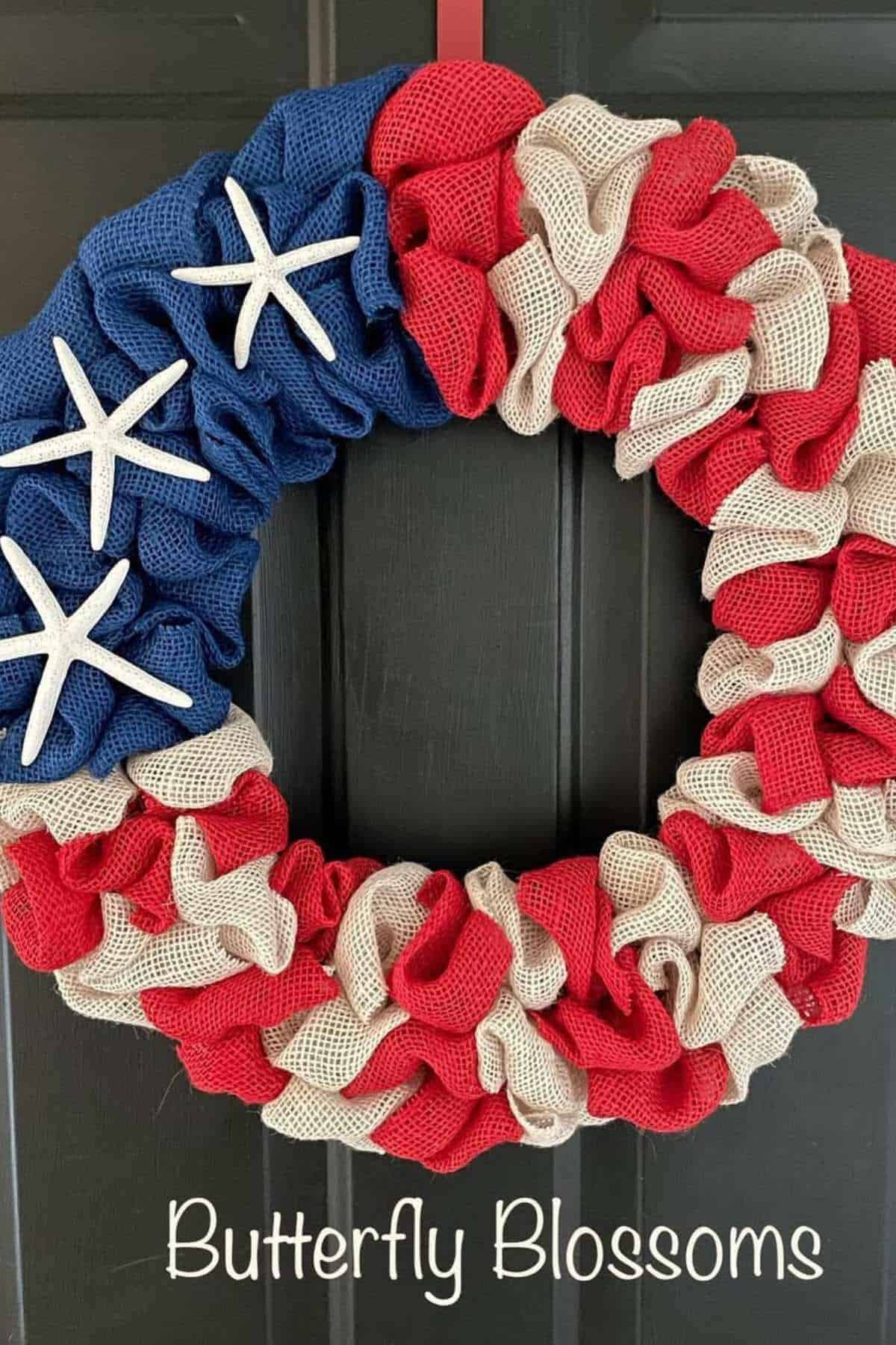 A patriotic wreath with blue, red, and white burlap, decorated with starfish, hangs on a door. "Butterfly Blossoms" is written at the bottom.