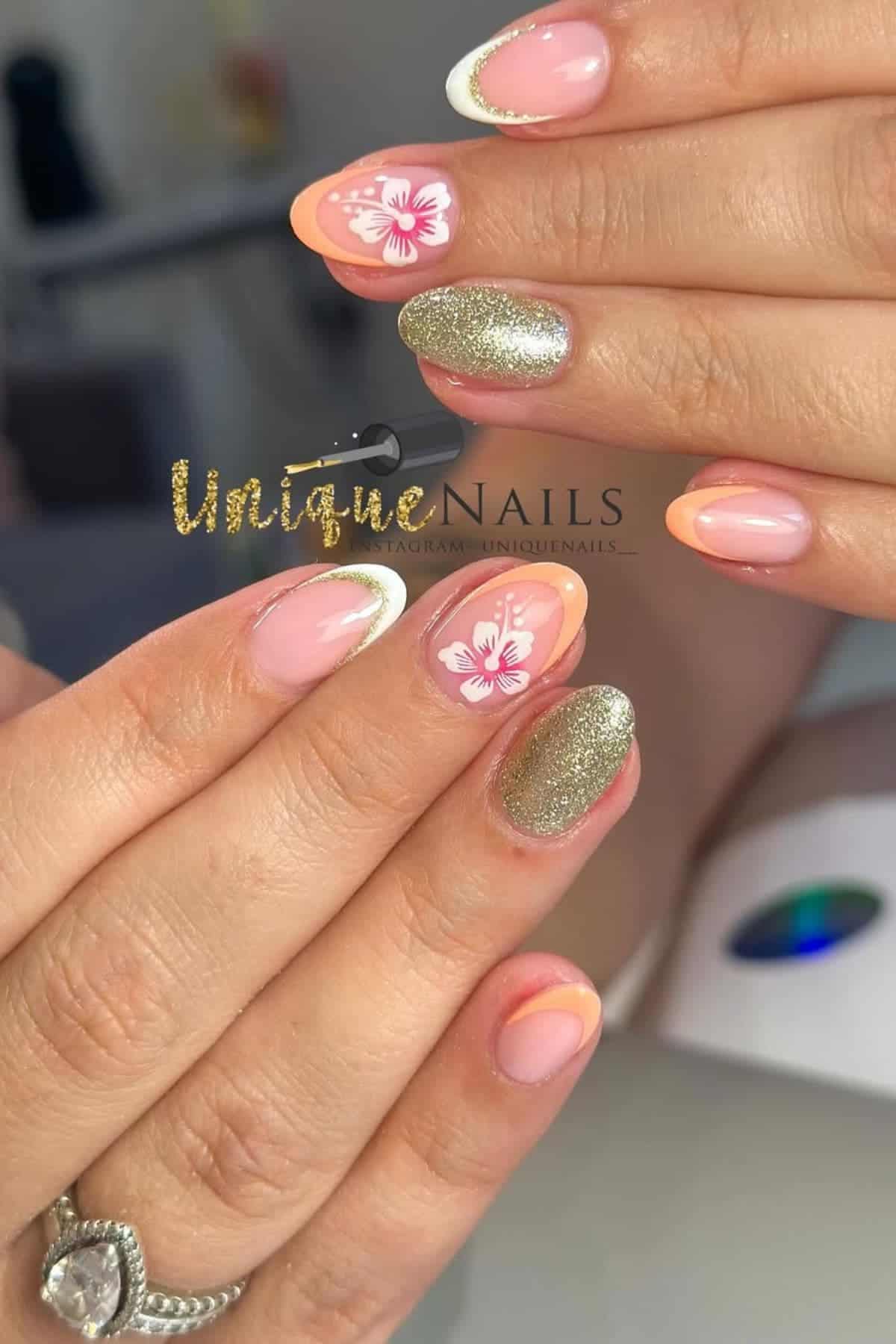 A hand with almond-shaped nails featuring pink floral designs, gold glitter, and orange-tipped French manicures.