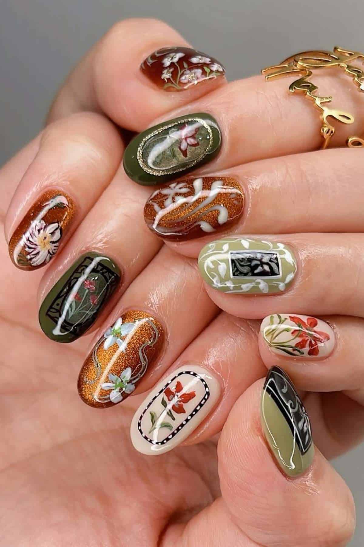 Close-up of a hand with long, almond-shaped nails featuring intricate floral and botanical designs in green, brown, white, and orange tones.