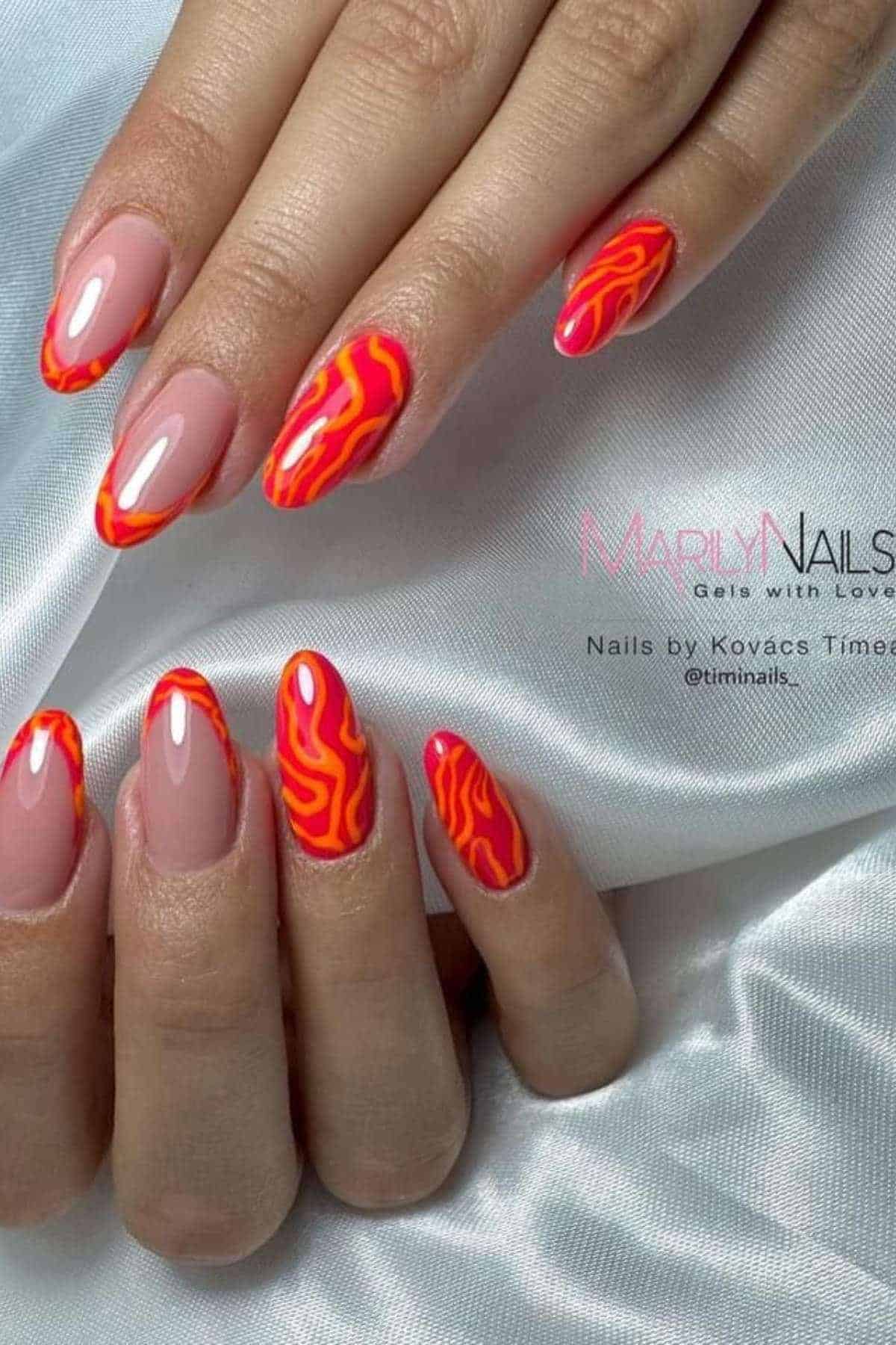 Hands with long almond-shaped nails featuring a nude base and bright orange and pink wavy line designs on the tips, displayed on a white satin fabric.